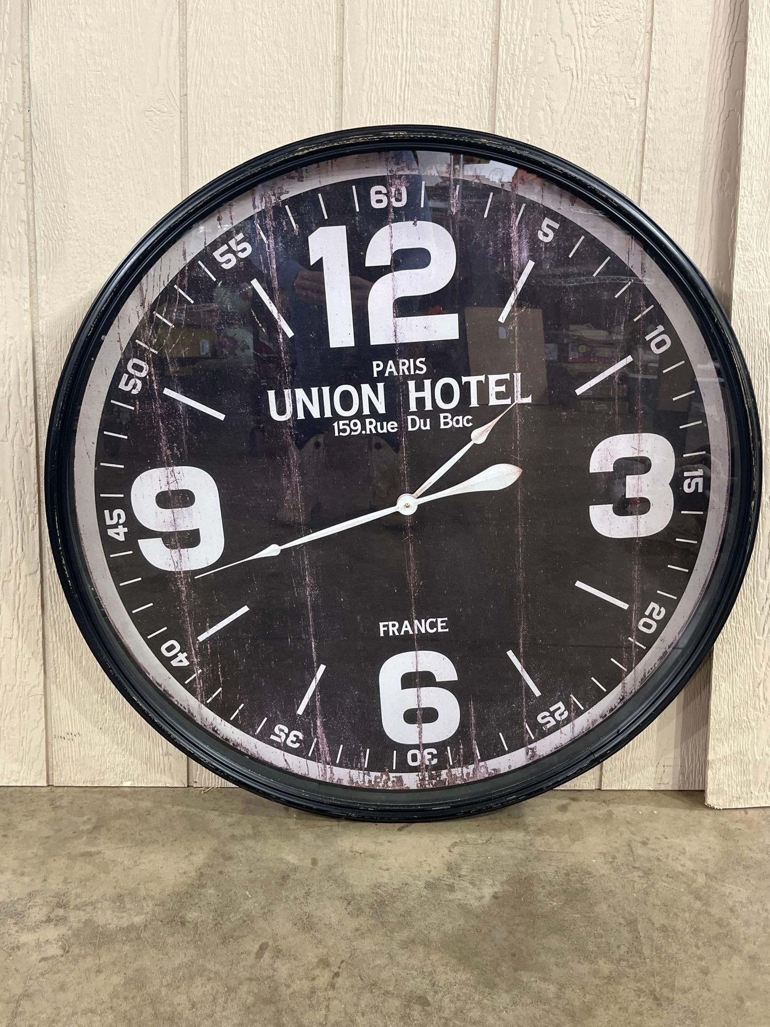 Couples in California Metal Wall Clock: A large circular wall clock featuring a distressed black metal frame and a glass face. The black dial is printed with white Arabic numerals at the 12, 3, 6, and 9 positions, surrounded by a minute