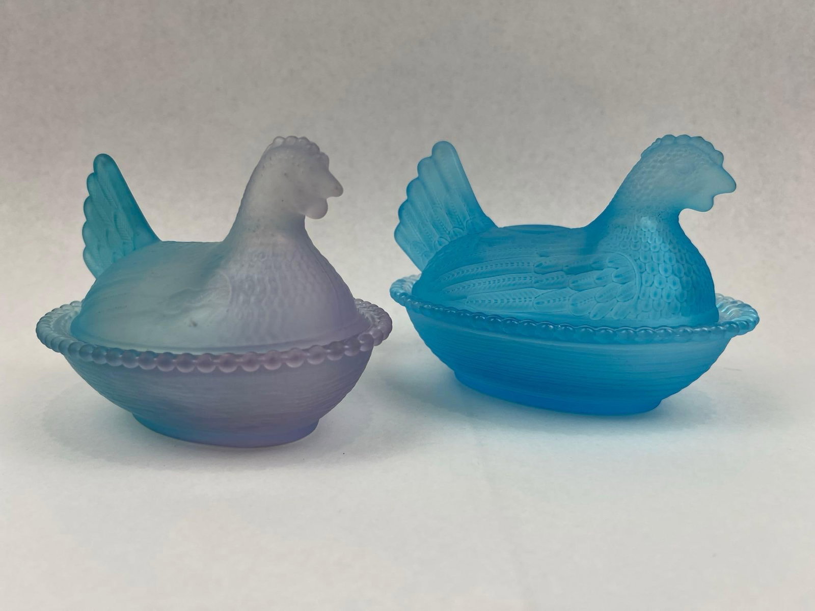Pair Frosted Satin Glass Hen on Nest: This pair of miniature covered dishes is crafted from frosted satin glass in the traditional "hen on nest" form. The collection includes one dish in a solid light blue color and a second piece