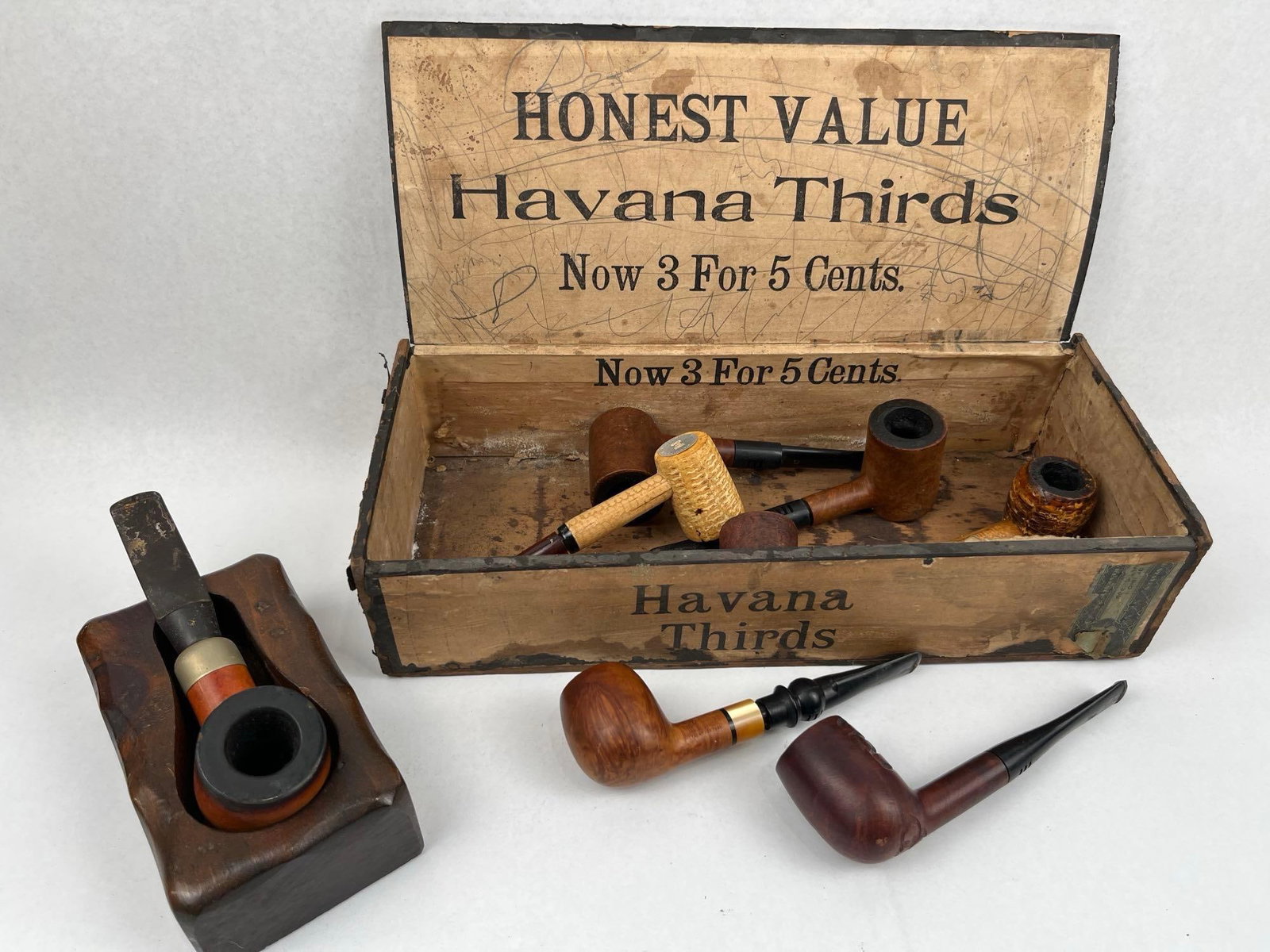 Pipes, Wood Pipe Rest & Havana Box: A collection of vintage tobacco smoking pipes accompanied by a rustic carved wooden pipe rest and a period storage box. The group includes several briar wood pipes and corn cob pipes with vulcanite