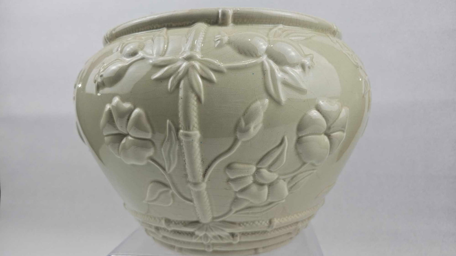 Relief Molded Botanical Ceramic Planter: This bulbous ceramic planter features a cream-colored glaze and is decorated with high-relief molded botanical motifs. The design includes vertical bamboo stalks that divide the body into sections