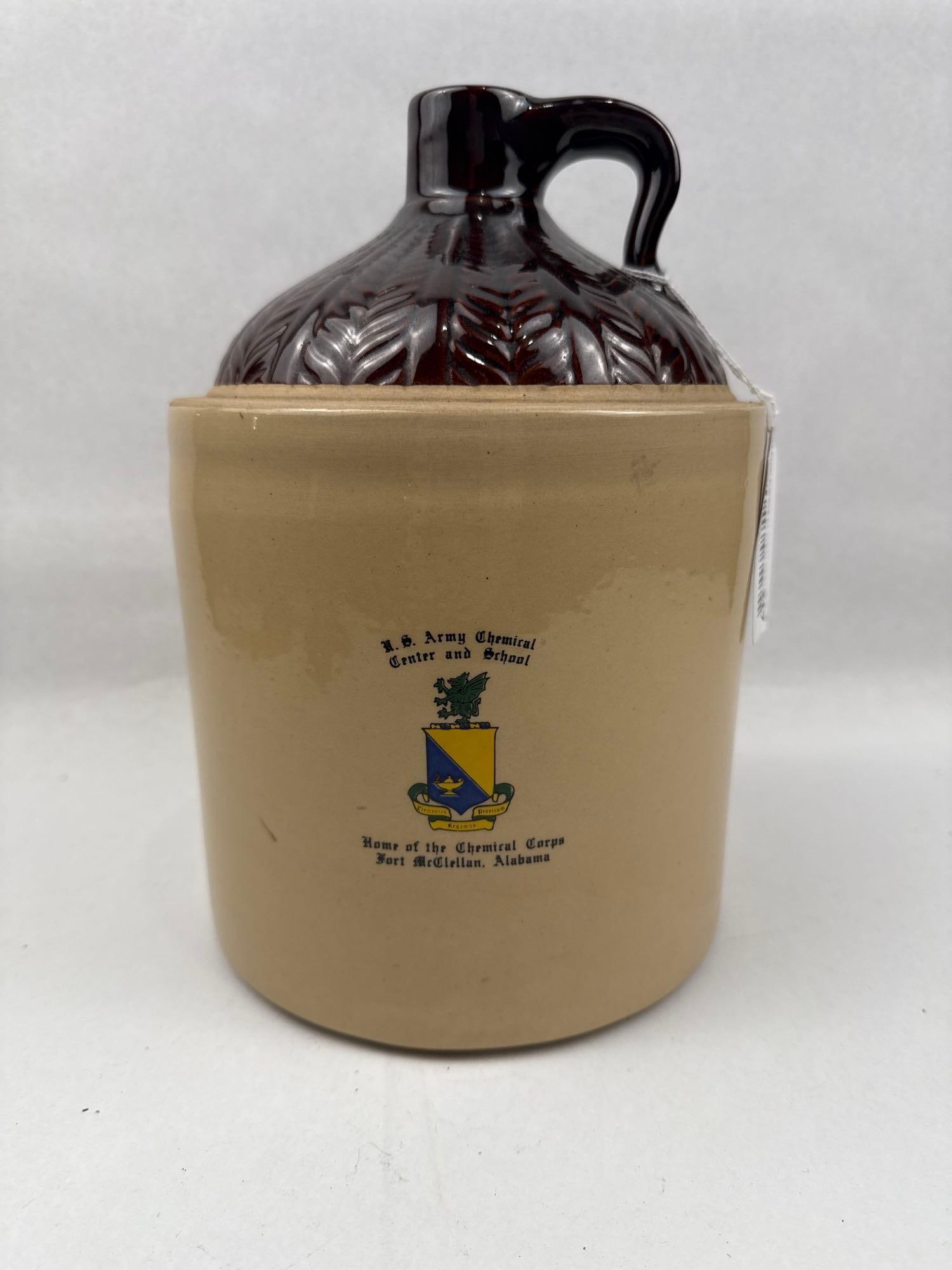 U.S. Army Chemical Corps Commemorative Stoneware Whiskey Jug: This commemorative stoneware whiskey jug features a cylindrical tan glazed body and a dark brown glazed shoulder molded with a repeating foliate leaf pattern. The front of the vessel bears a