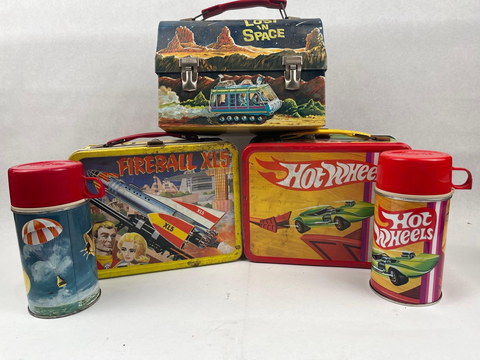 Space & Racing Metal Lunchbox Set: This collection consists of lithographed tin lunchboxes and plastic-capped thermoses featuring popular mid-20th-century entertainment properties. The group includes a dome-top lunchbox with graphics