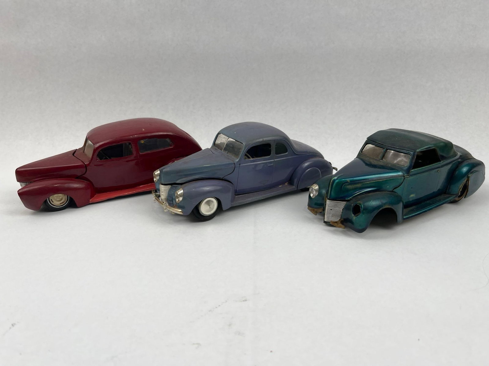 3 1940 Ford Models & Ideal Toy Slot Car: A trio of vintage 1940-style Ford model cars in various body styles and configurations. The group includes a metallic green convertible coupe, a hand-painted red two-door sedan, and a blue-gray five-w