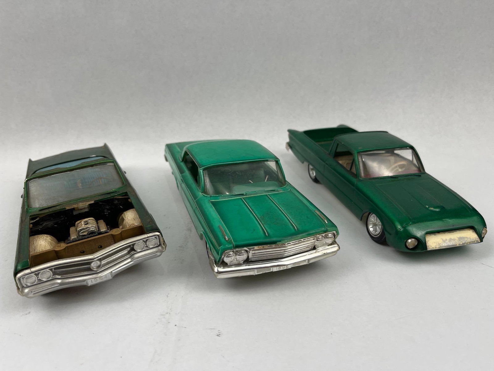 3 1:25 Plastic Emerald Model Cars: A group of three vintage 1:25 scale plastic model cars, all finished in a coordinating metallic emerald green. The collection consists of a hardtop model with molded script on the rear quarter panels