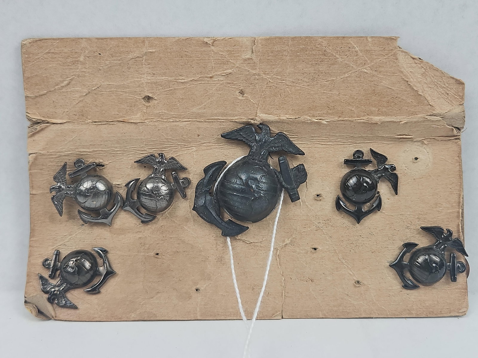 USMC Eagle Globe & Anchor Insignia: A collection of United States Marine Corps insignia depicting the traditional Eagle, Globe, and Anchor motif. The group consists of a larger central cap device and several smaller collar-sized pins.