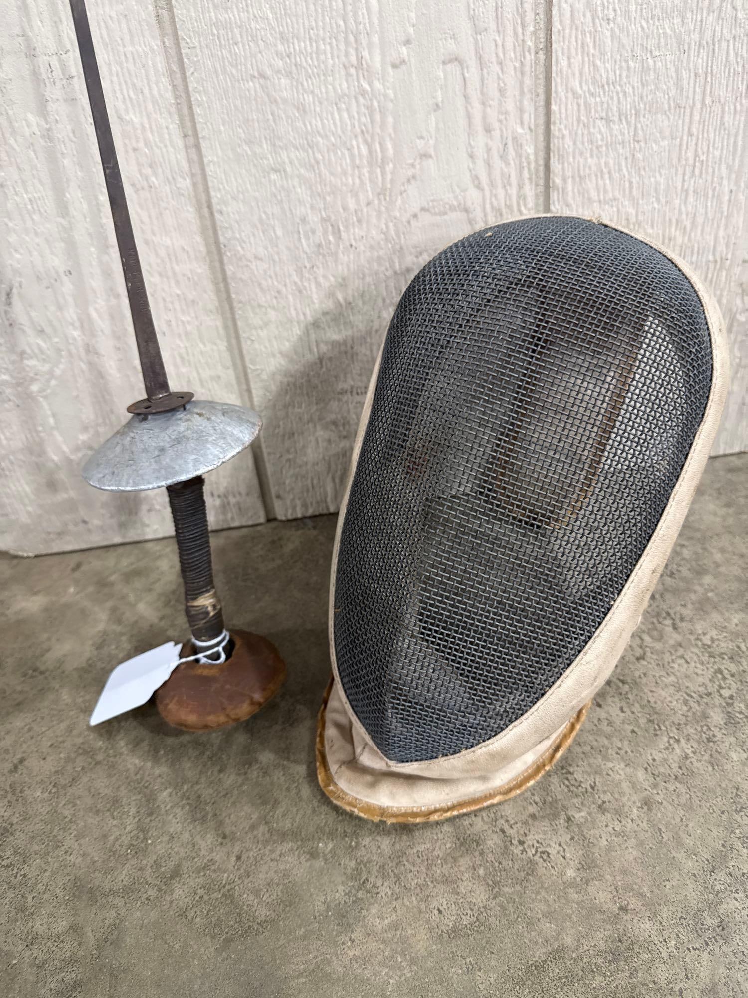 Two French Fencing Items: A French fencing foil and protective mask. The foil features a metallic bell guard, a dark cord-wrapped grip, and a large rounded pommel. The blade is impressed with the characters MADE IN FRANCE in