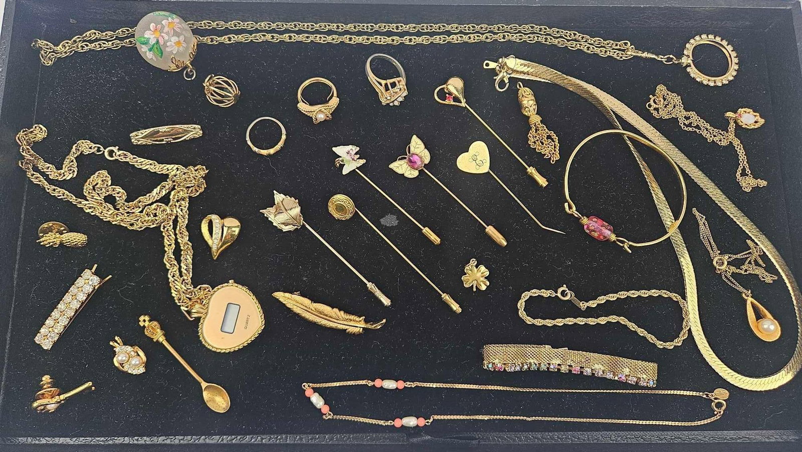 Avon Gold Toned Jewelry & Stickpins: This lot comprises a variety of gold-toned costume jewelry including necklaces, bracelets, rings, and pins. A notable piece is a heart-shaped digital watch pendant featuring a dial marked with the