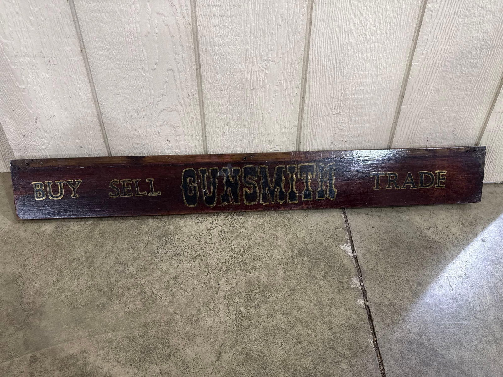 Hand-Painted Wooden Gunsmith Trade Sign: A rectangular wooden trade sign for a gunsmith, featuring a dark reddish-brown stained finish and hand-painted lettering. The central portion displays the word GUNSMITH in large, stylized black block