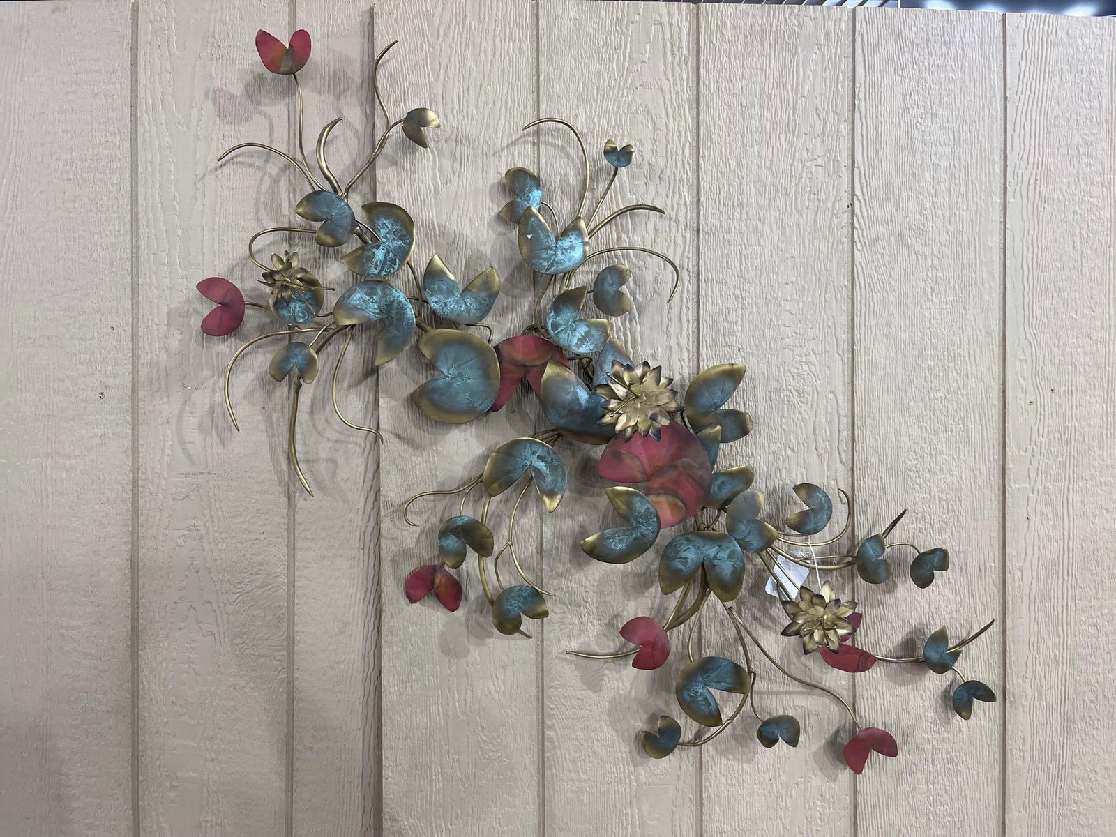 Patinated Metal Botanical Sculpture: A large decorative wall sculpture composed of brass-toned metal wire and sheet metal in a botanical design. The piece features arching vines adorned with stylized lotus blossoms and lily pads. The sma