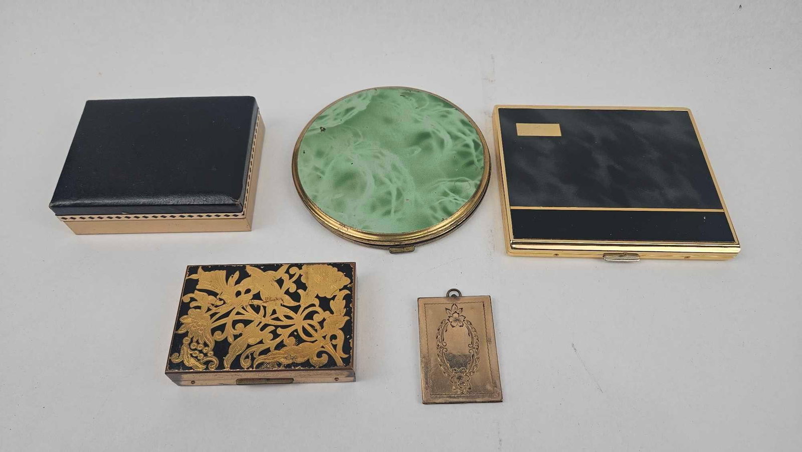 Elgin American & Colibri Vanity Set: A collection of vintage personal accessories and vanity items. The group includes a rectangular American vanity case featuring a gold-tone floral and bird motif over a black ground. The interior lid