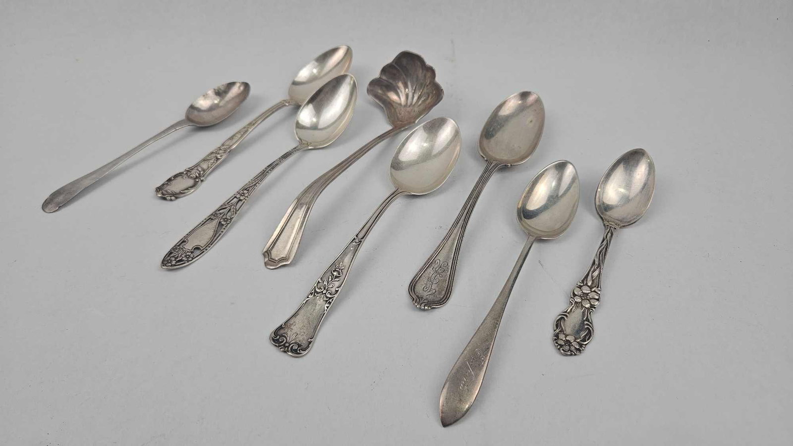 Sterling Silver Flatware Collection: A collection of sterling silver flatware featuring several spoons and a ladle with a shell-form bowl. The assortment exhibits a variety of late 19th and early 20th-century decorative styles,