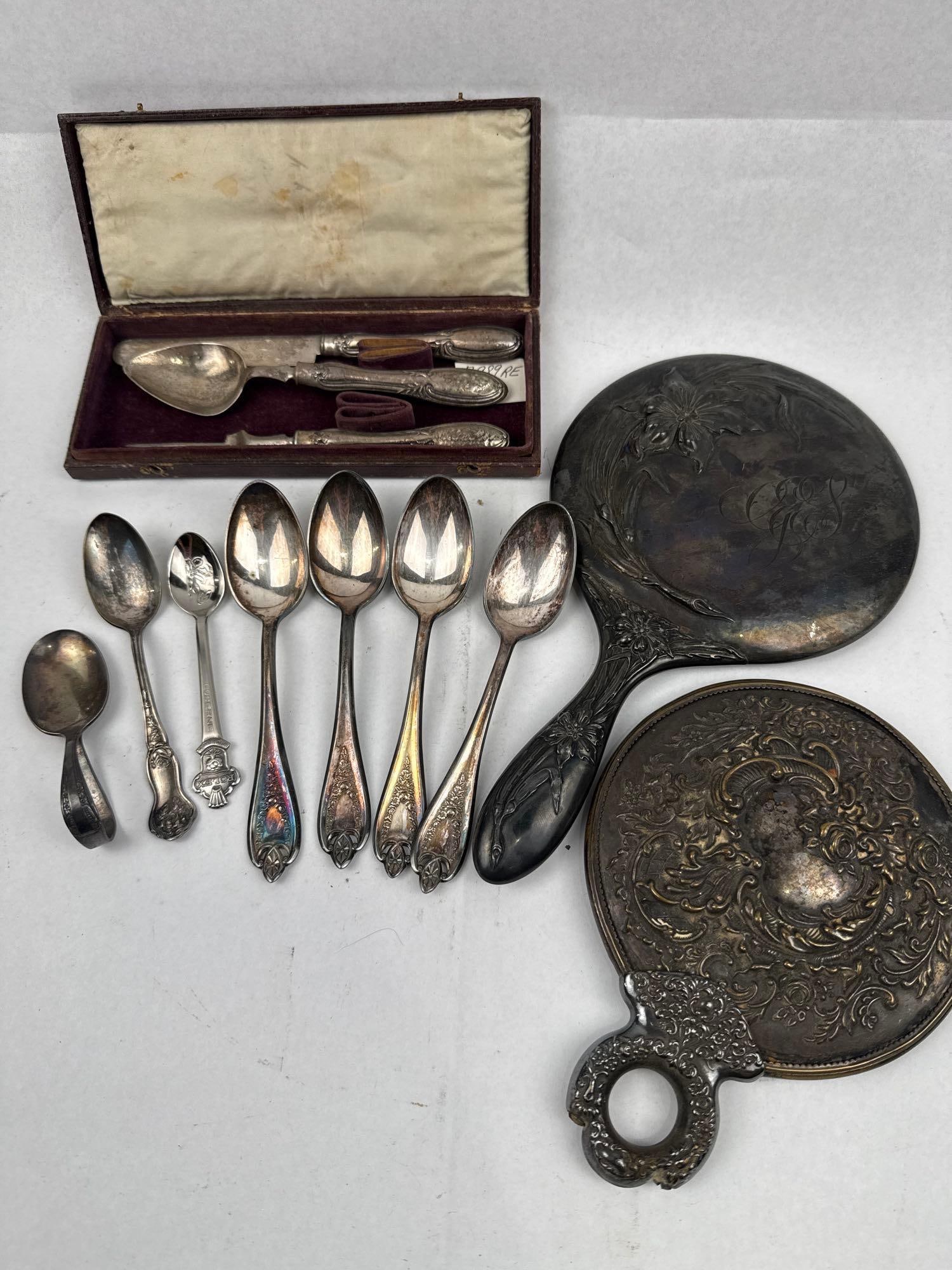 Unger Brothers & Fessenden Silver Items: An assortment of silver and silver-plated items, including two hand mirrors, a boxed youth set, and various table and souvenir spoons. The largest hand mirror features an Art Nouveau style floral