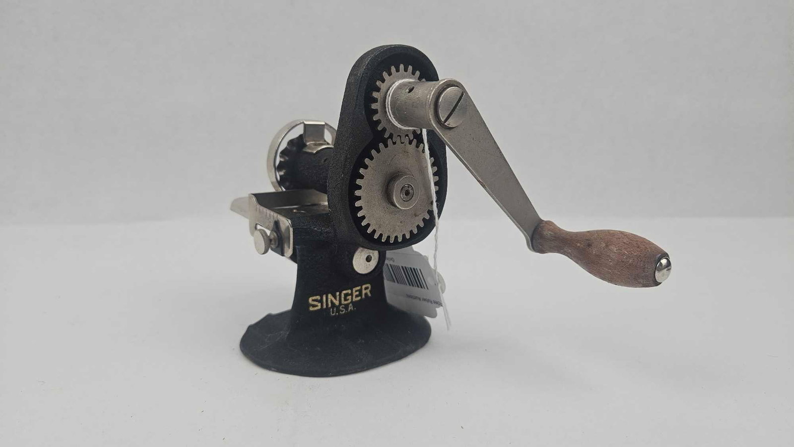 1930s Singer Cast Iron Pinking Machine: An American hand-operated pinking machine produced by Singer. The unit is constructed from cast iron with a black crinkle finish and features a hand crank with a turned wooden handle. The mechanism