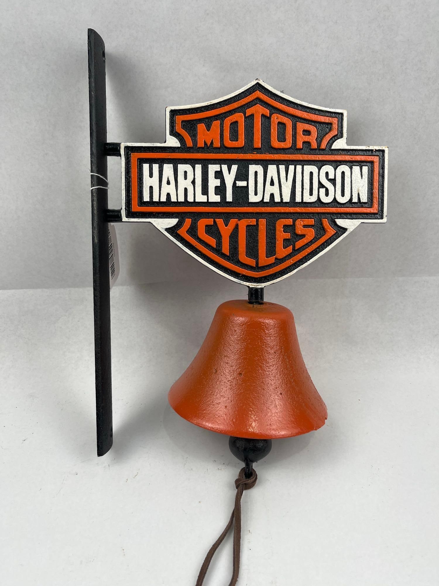 Harley-Davidson Cast Metal Wall Bell: A cast metal wall-mounted bell featuring a decorative plaque in the form of a bar and shield. The plaque is finished in orange, black, and white with raised lettering. The upper section of the shield