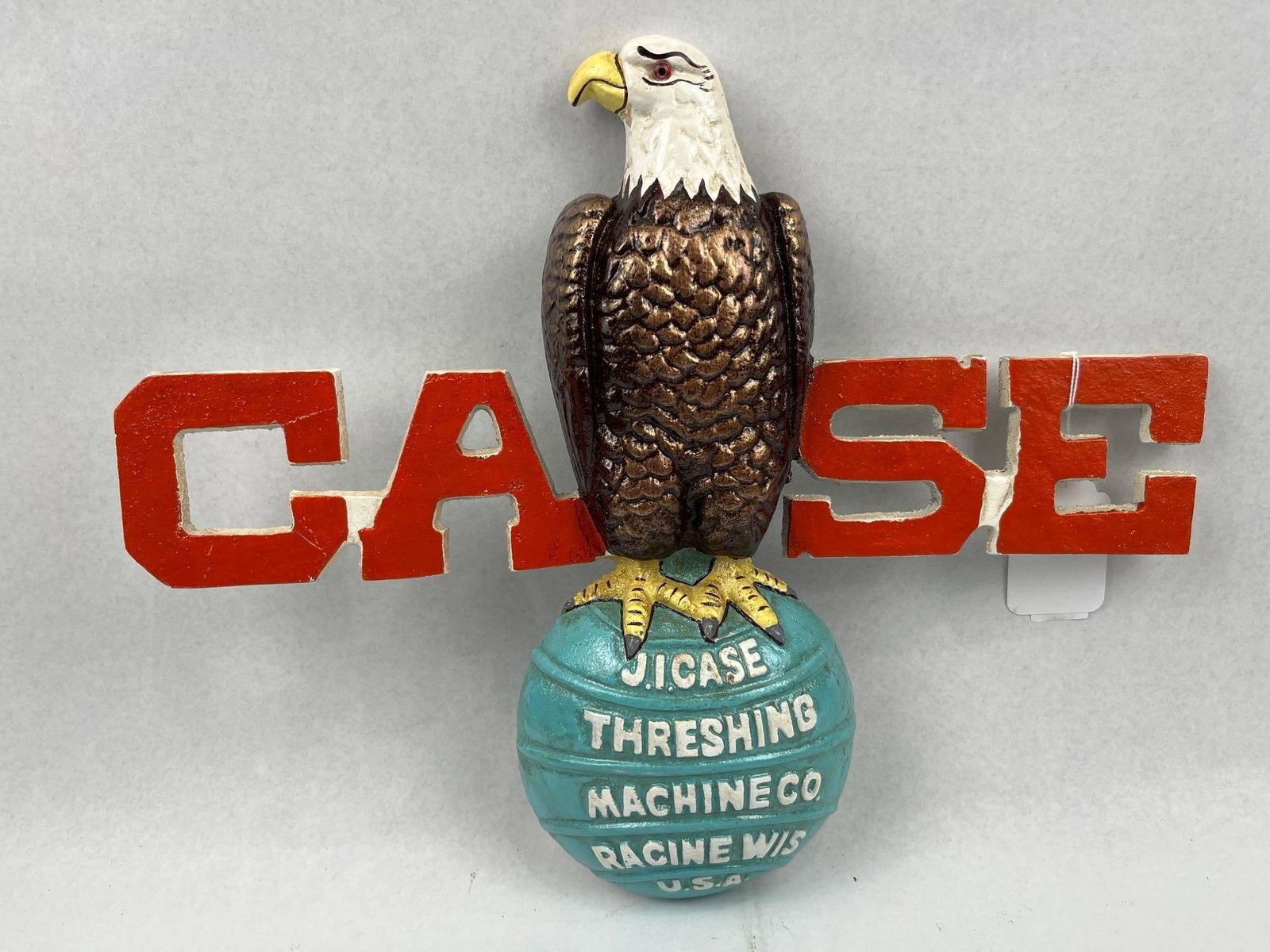 J.I. Case Cast Metal Advertising Plaque: A polychrome painted cast metal advertising wall plaque for the J.I. Case Threshing Machine Co. The piece features the company mascot, the Old Abe eagle, perched atop a globe and set against large red