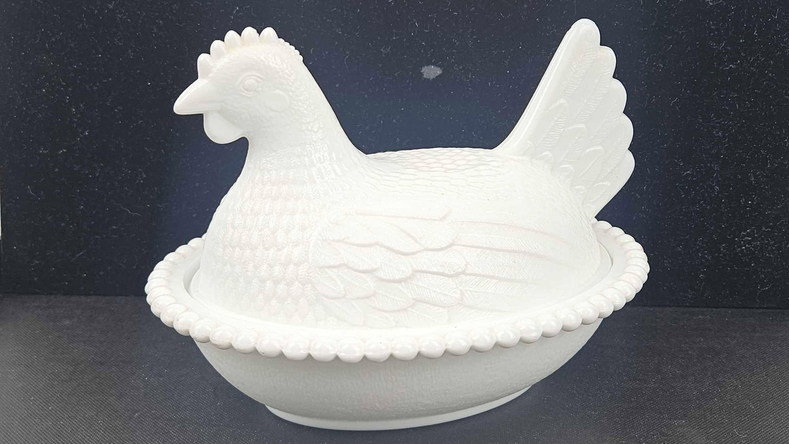 Iridescent Milk Glass Hen on Nest Dish: A two-piece covered dish constructed of opaque white milk glass with a pearlized iridescent finish throughout. The lid is molded in the form of a nesting hen with detailed plumage and a raised tail.