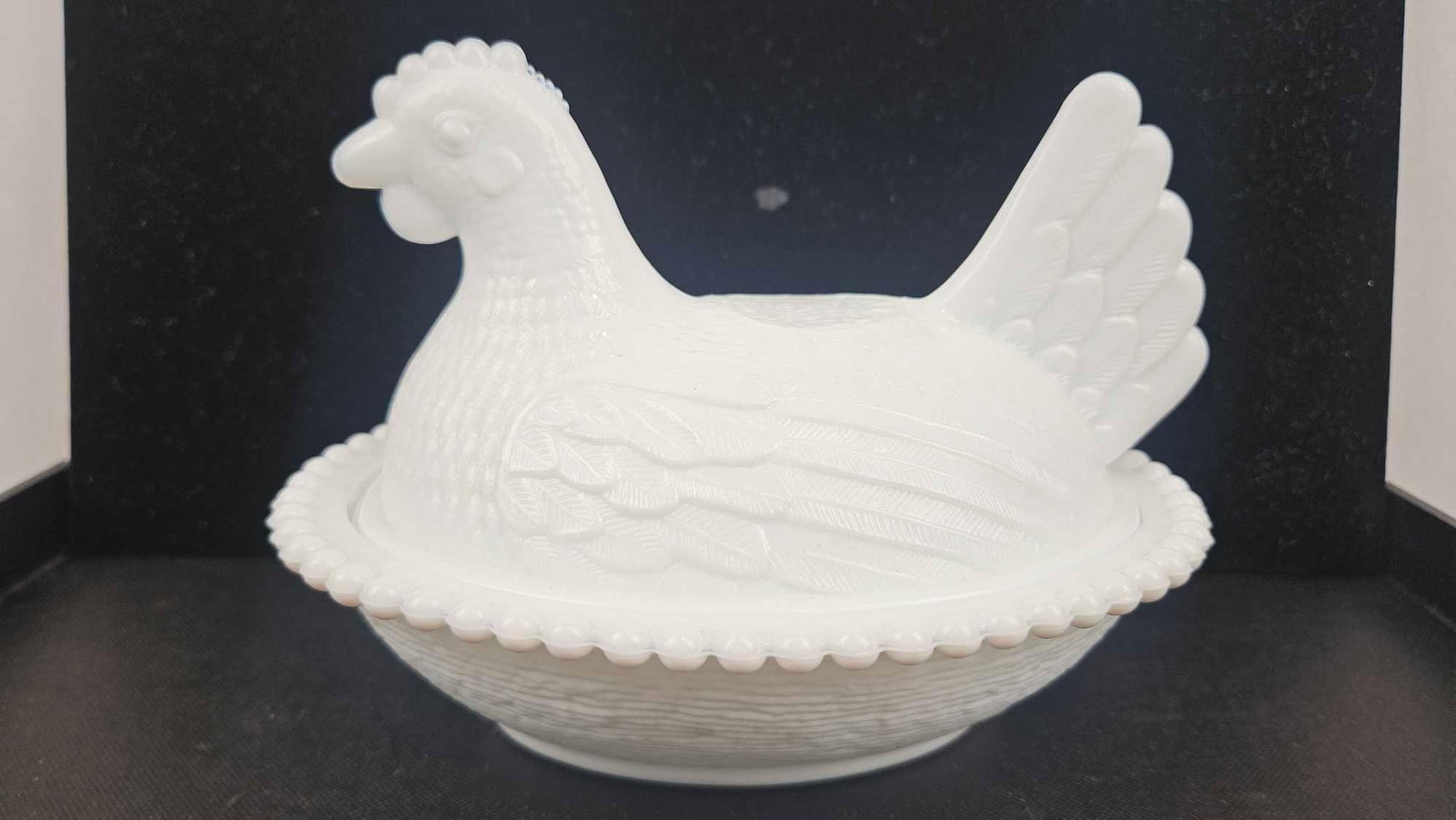 Milk Glass Hen on Nest Covered Dish: A two-part white milk glass covered dish featuring a figural lid in the form of a seated hen and a corresponding base. The lid is molded with detailed plumage on the wings, tail, and body,