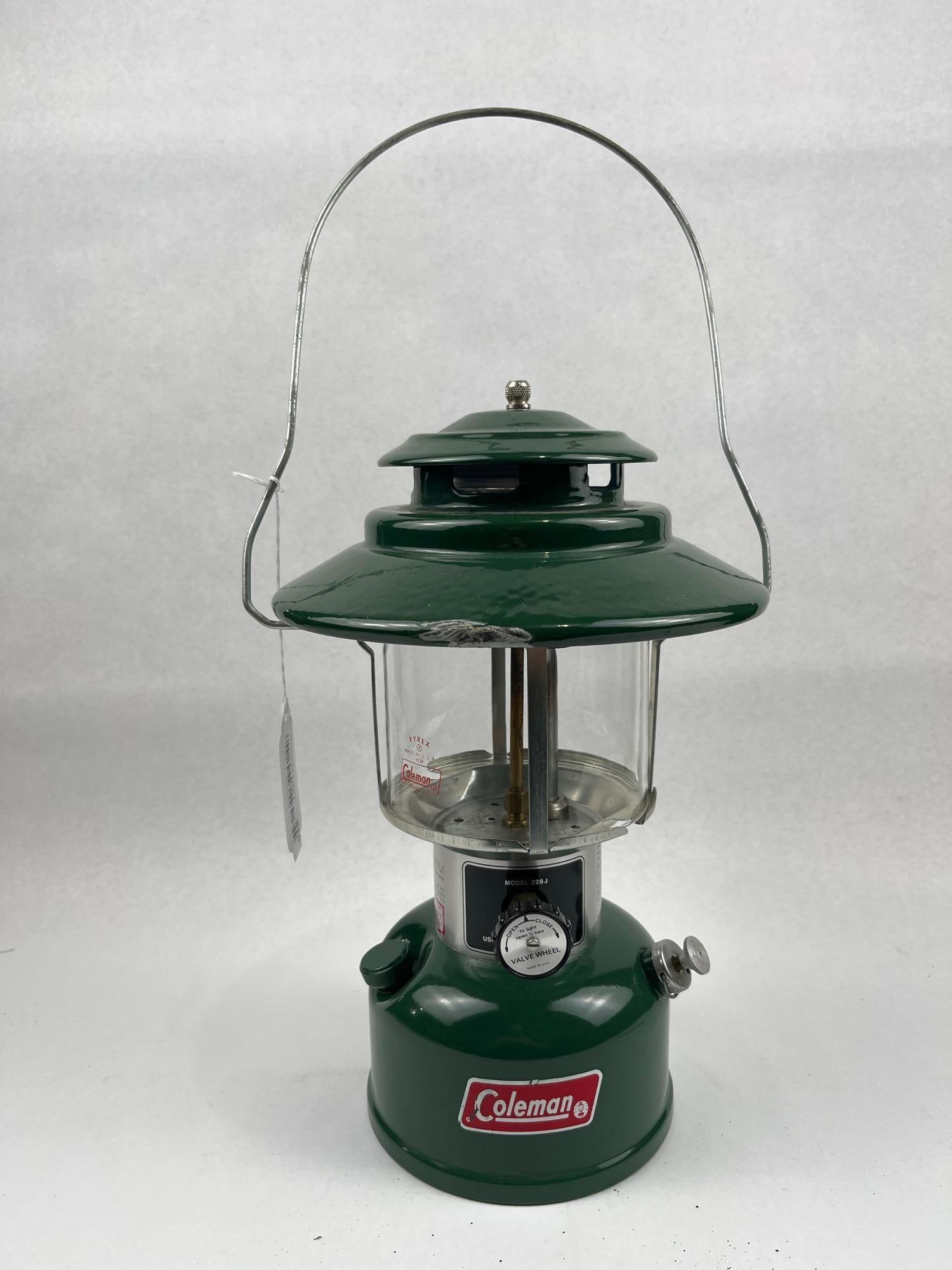 Coleman 228J Liquid Fuel Lantern 1976: A liquid fuel camping lantern featuring a dark green porcelain enamel ventilator of the wide-brimmed big hat variety atop a matching green steel fount. The clear glass globe is printed with a red logo