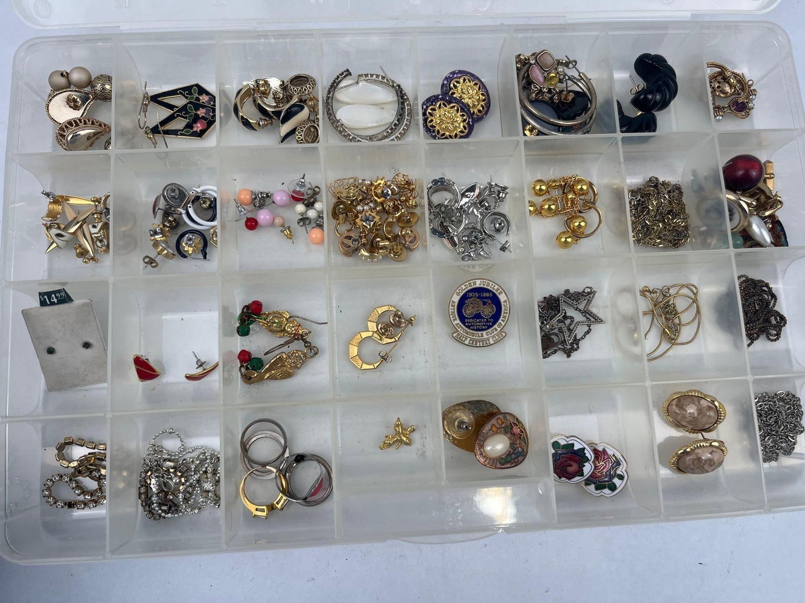 Assorted Vintage Costume Jewelry: A diverse collection of costume jewelry presented in a multi-compartment clear plastic storage box. The group features various styles ranging from mid-century vintage to modern pieces, constructed fro