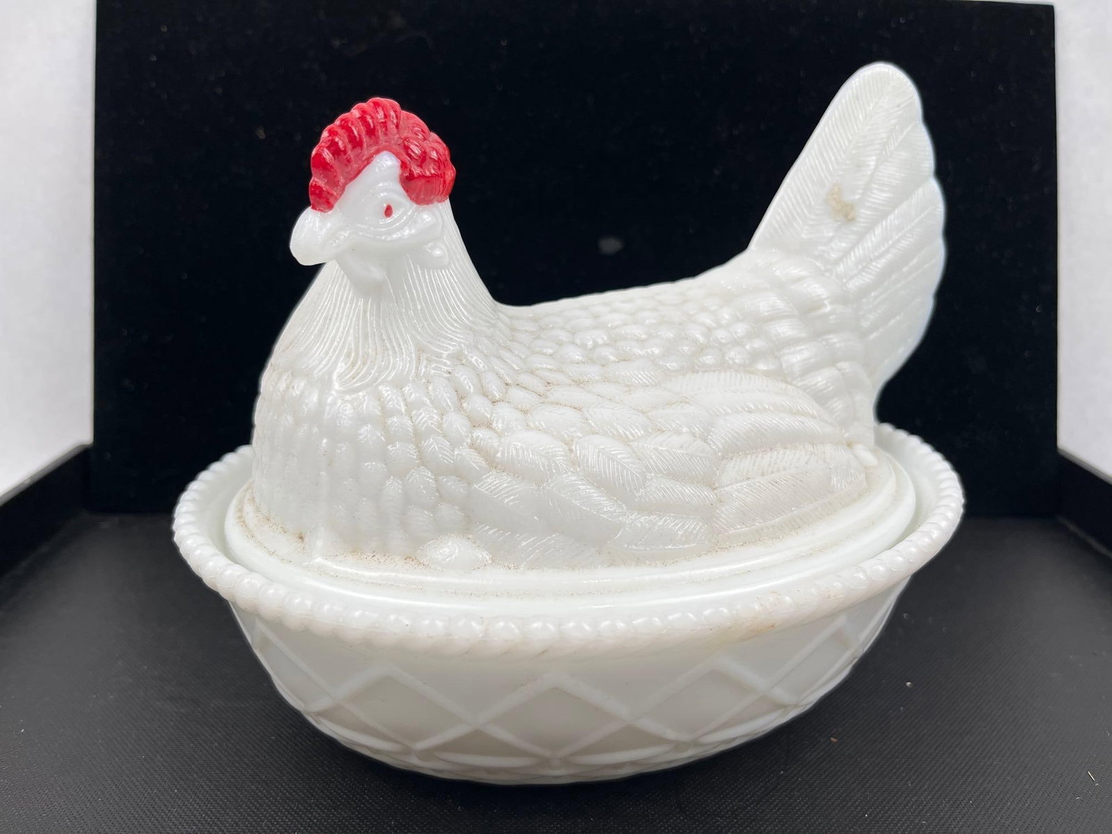 Milk Glass Hen on Nest Covered Dish: A white milk glass covered dish featuring a lid modeled in the form of a seated hen with an oval base. The hen lid displays textured feather detailing and red cold-painted accents to the comb and eyes