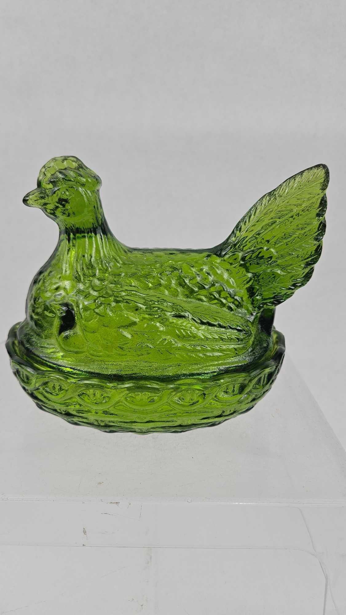 Green Pressed Glass Hen on Nest Dish: This miniature two-piece covered dish is composed of translucent vibrant green pressed glass. The lid is molded in the form of a seated hen, featuring detailed plumage, a prominent comb, and a wattle.