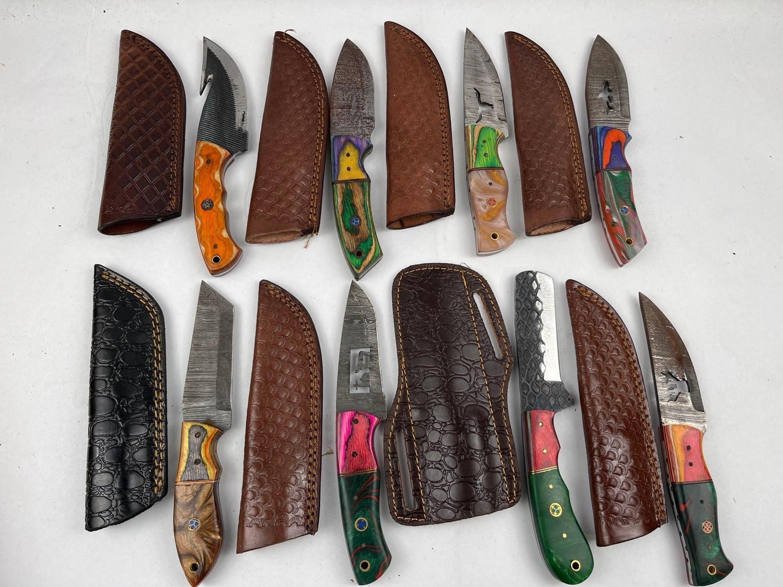 Damascus Steel & Mixed Media Knives: This lot consists of a collection of artisanal fixed-blade knives, each accompanied by a coordinating leather sheath. The blades feature a variety of constructions and finishes, including