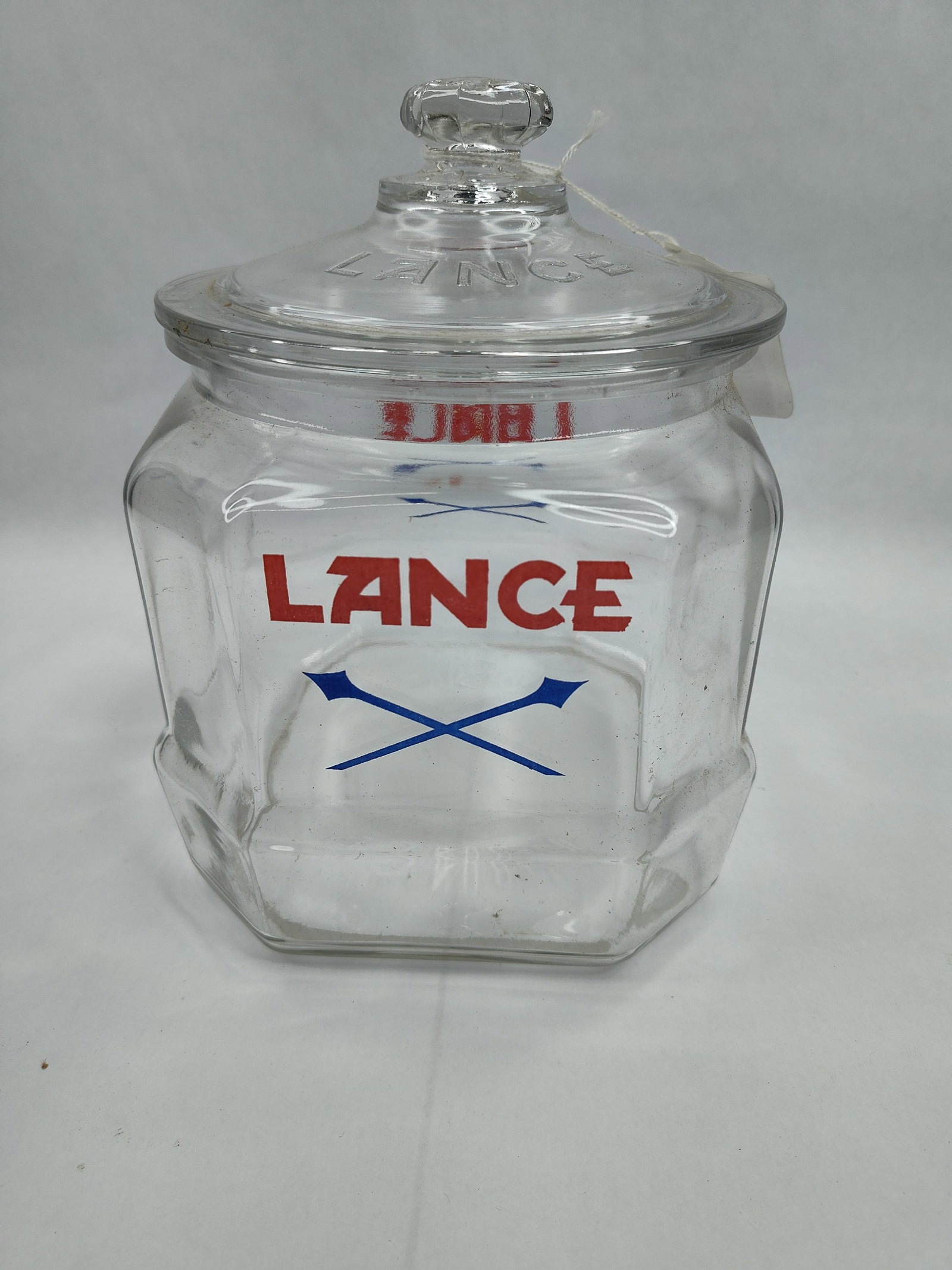 Lance Octagonal Glass Counter Jar: This store counter jar is constructed from clear glass with an eight-sided octagonal body. The jar is accompanied by a matching glass lid featuring a faceted knob handle. The front and back of the