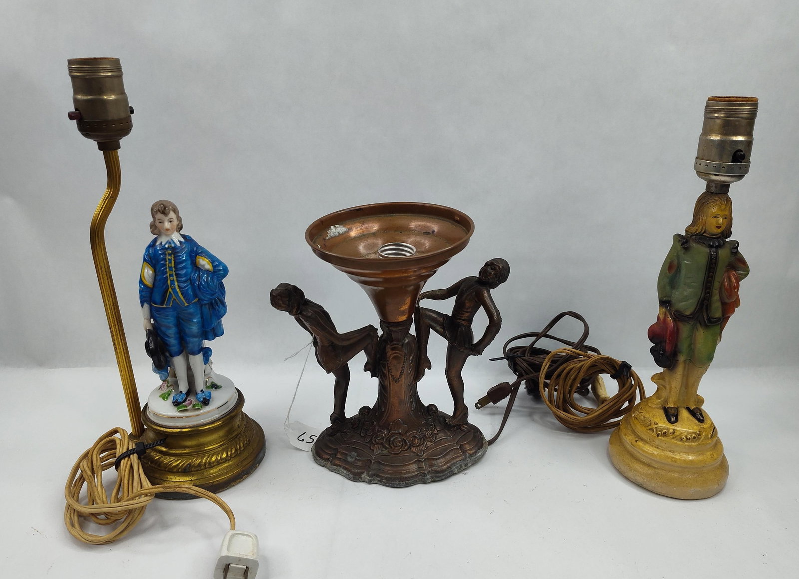 Set 3 Figural Porc. & Metal Lamps: A group of three decorative table lamps of varying materials and styles. The first lamp features a glazed porcelain figure of a boy in blue 18th-century attire standing on a base with floral accents,