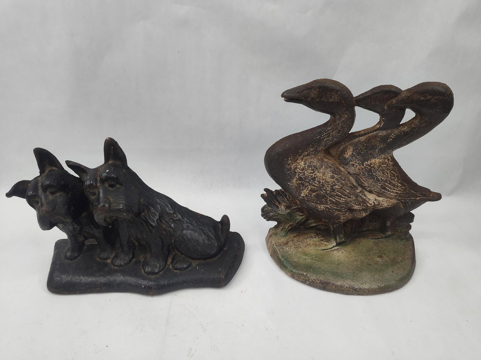 Two Cast Iron Animal Figure Doorstops: This lot features two cast metal doorstops, each cast with a hollow reverse and a flat base intended for weighted stability. The first figure depicts a pair of seated Scottish Terrier dogs, finished