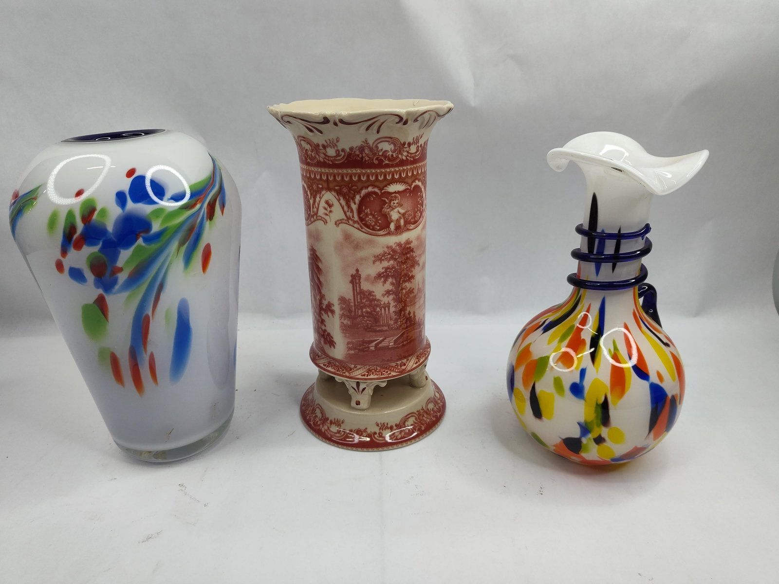 Set of 3 Glass & Ceramic Vases: A trio of decorative vessels comprising two hand-blown art glass vases and one footed ceramic vase. The first glass vase features a tapered, ovoid form in opaque white glass, decorated with an express