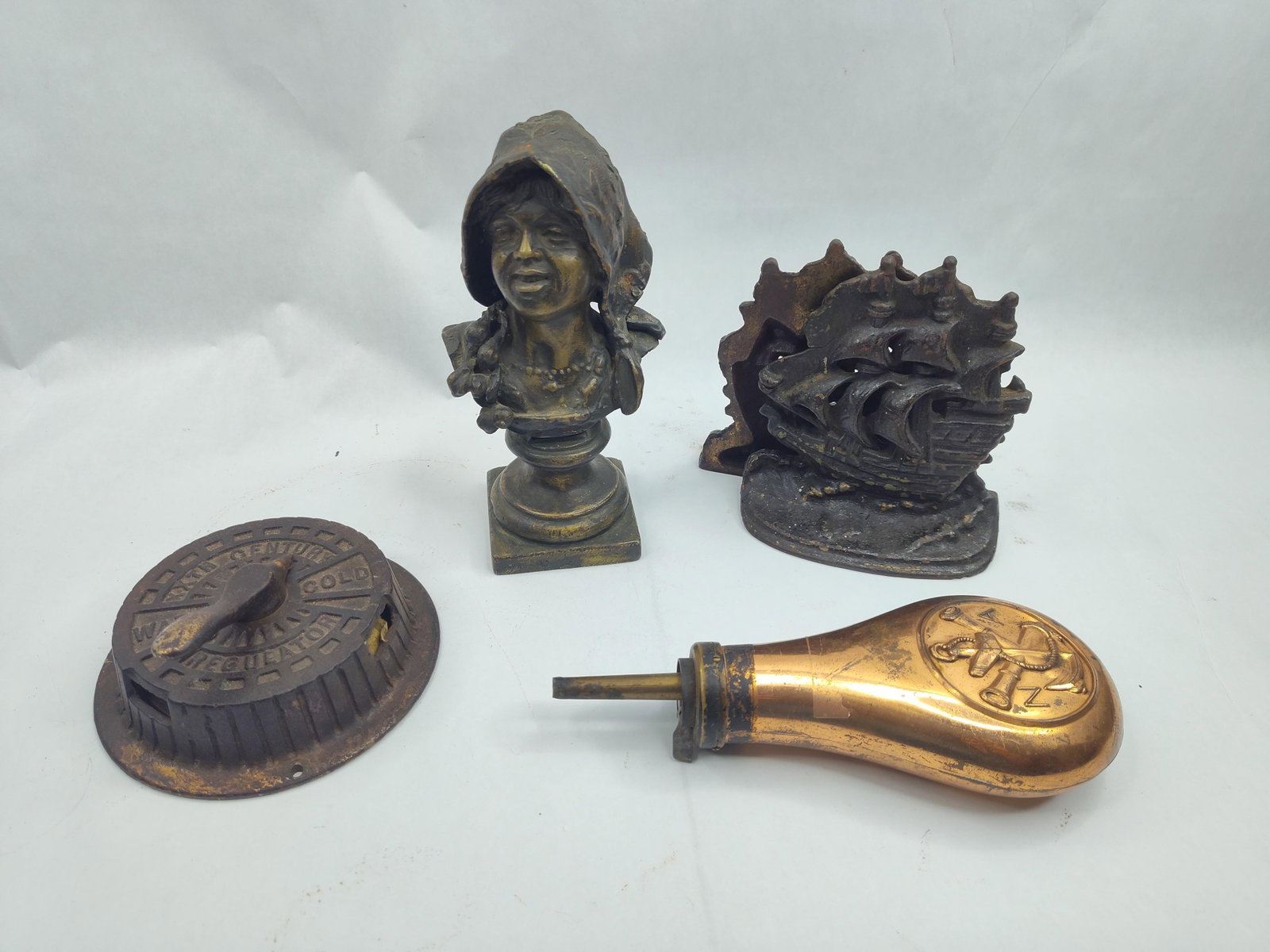 Cast Metal Powder Flask & Plate: A collection of assorted cast metal antiques and decorative objects. The lot includes a cast iron bust of a young girl wearing a floral-patterned hood or bonnet with braided hair, finished with a