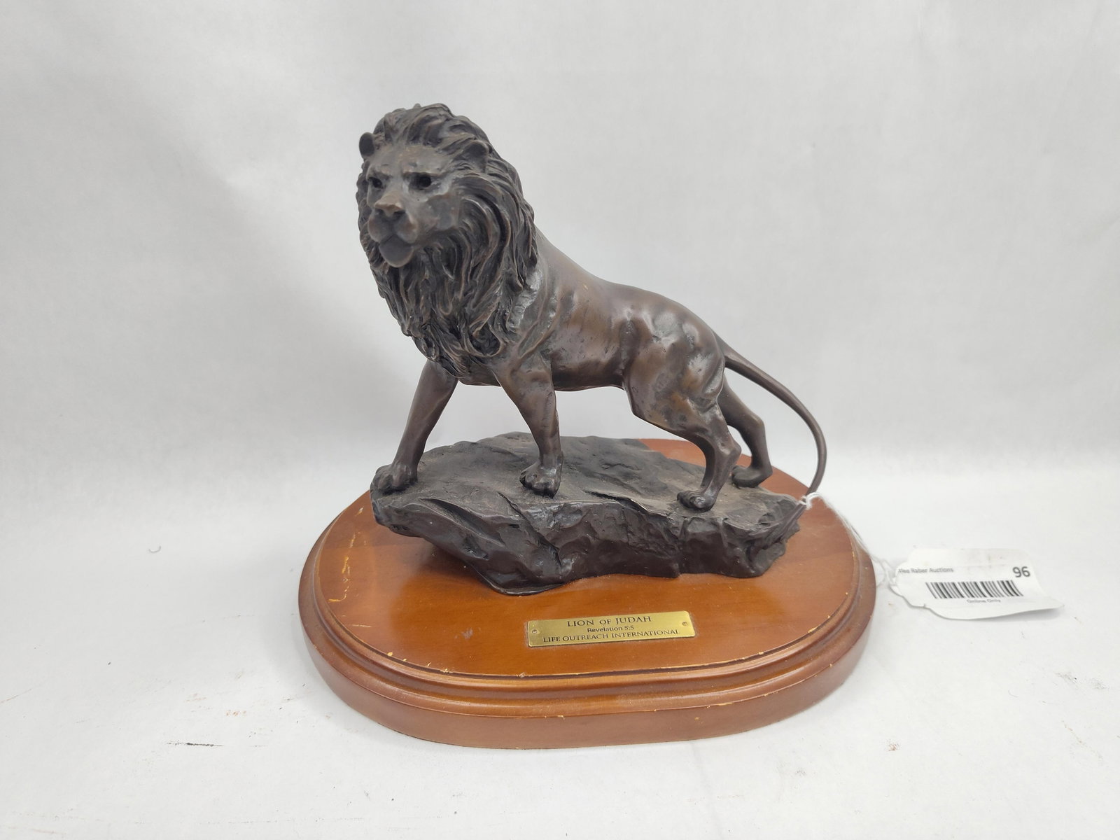 Lion of Judah Metal Sculpture w/ Base: A dark brown patinated cast metal sculpture of a standing male lion, realistically modeled with a thick textured mane. The lion is depicted in a walking pose atop a stylized rocky outcrop. The entire