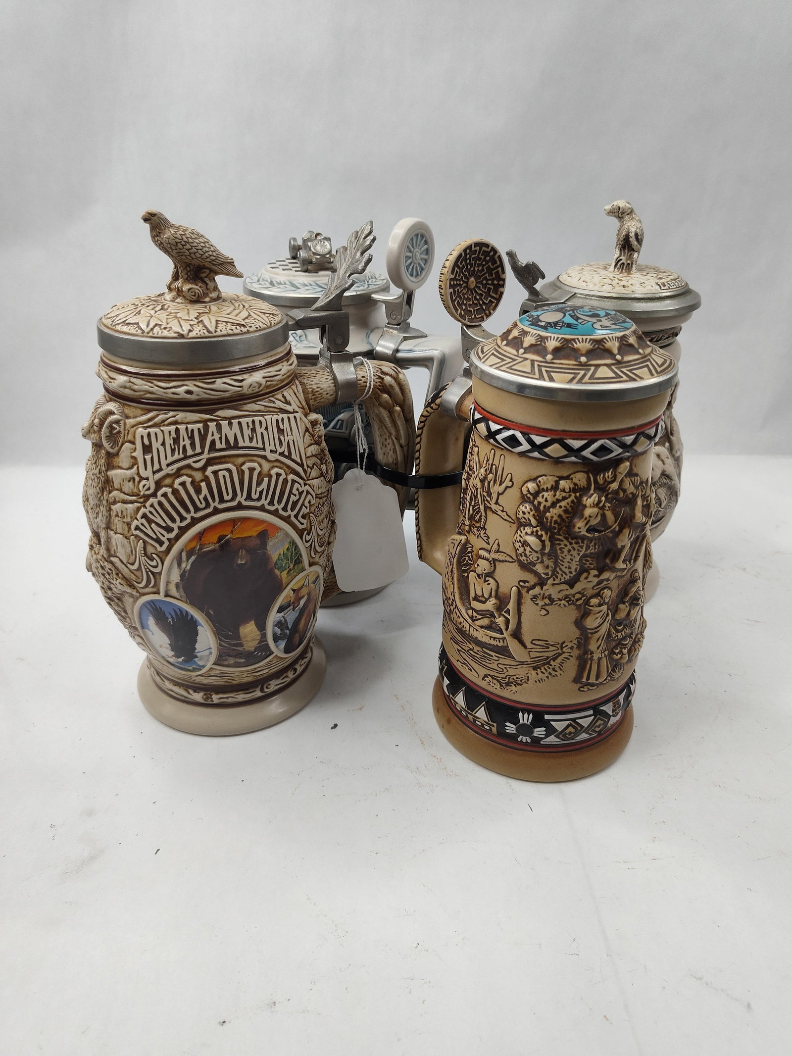 Set 4 Avon Brazilian Ceramic Steins: A collection of four ceramic beer steins featuring high-relief molded decoration and metal-hinged lids. Each stein is decorated with a specific thematic wrap-around scene. The first features a central