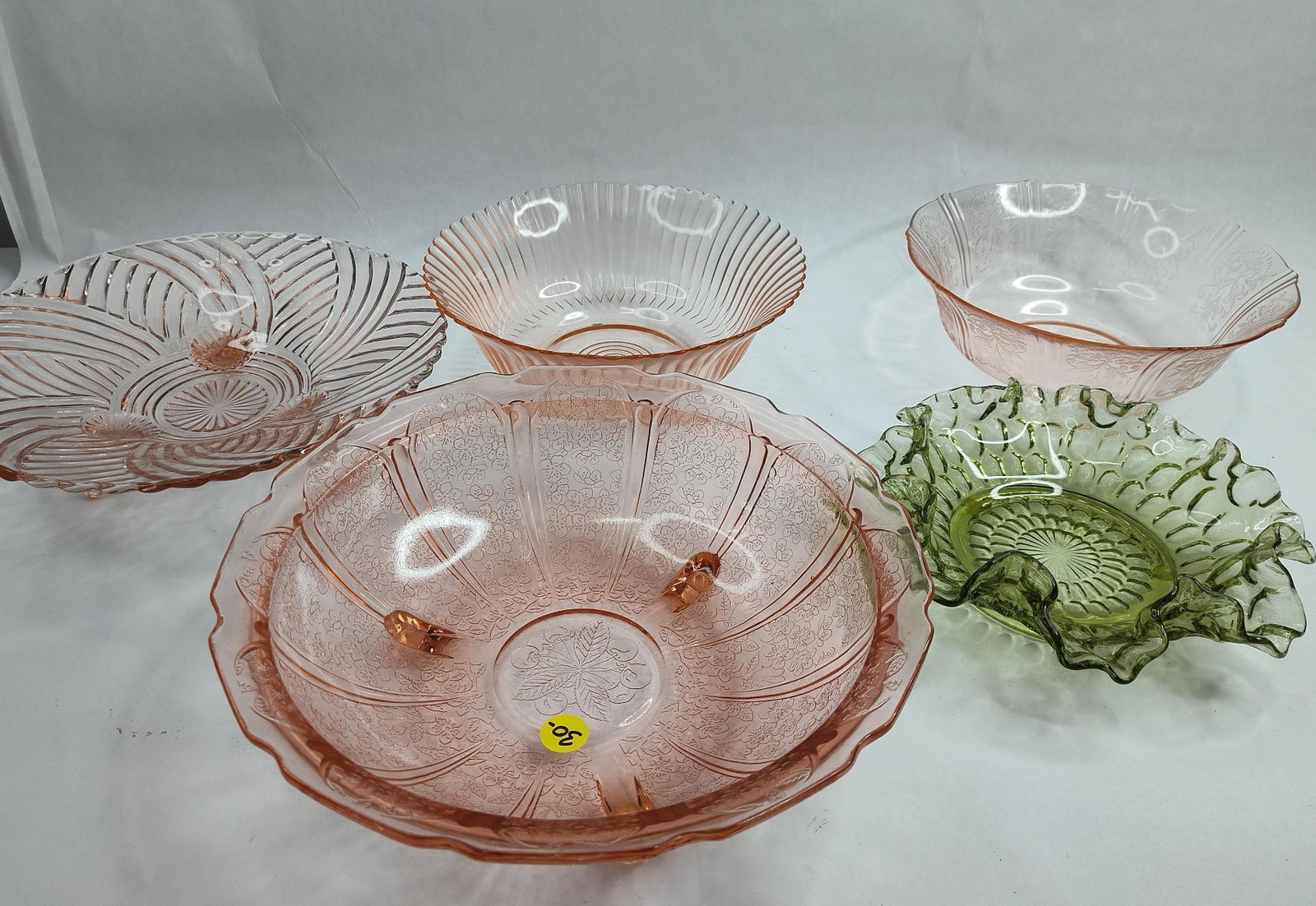 Pink & Green Depression Glassware: A collection of translucent pressed glassware from the American Depression era and periods, consisting primarily of pink glass with one green specimen. The grouping includes a large pink footed bowl f