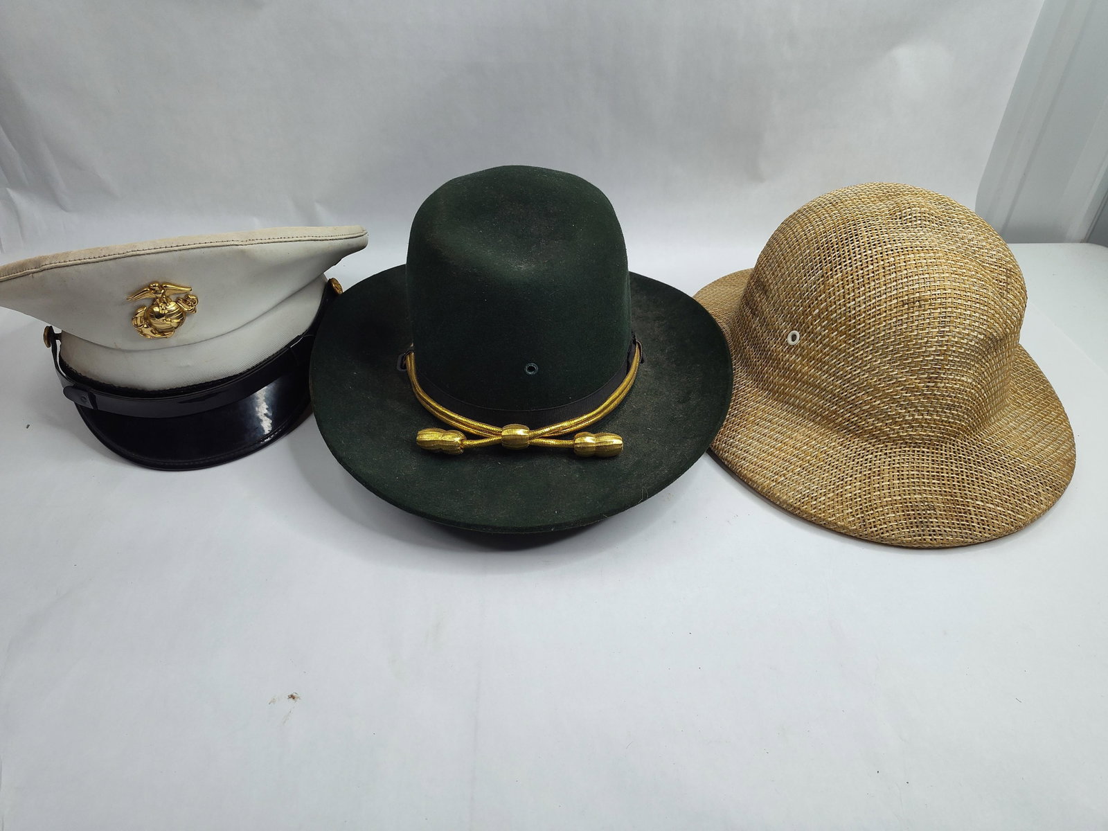 Trio of Military & Utility Headgear: This lot comprises three pieces of headgear. The first is a United States Marine Corps officer's white service cap. It features a gold-toned metal Eagle, Globe, and Anchor insignia on the front and a 