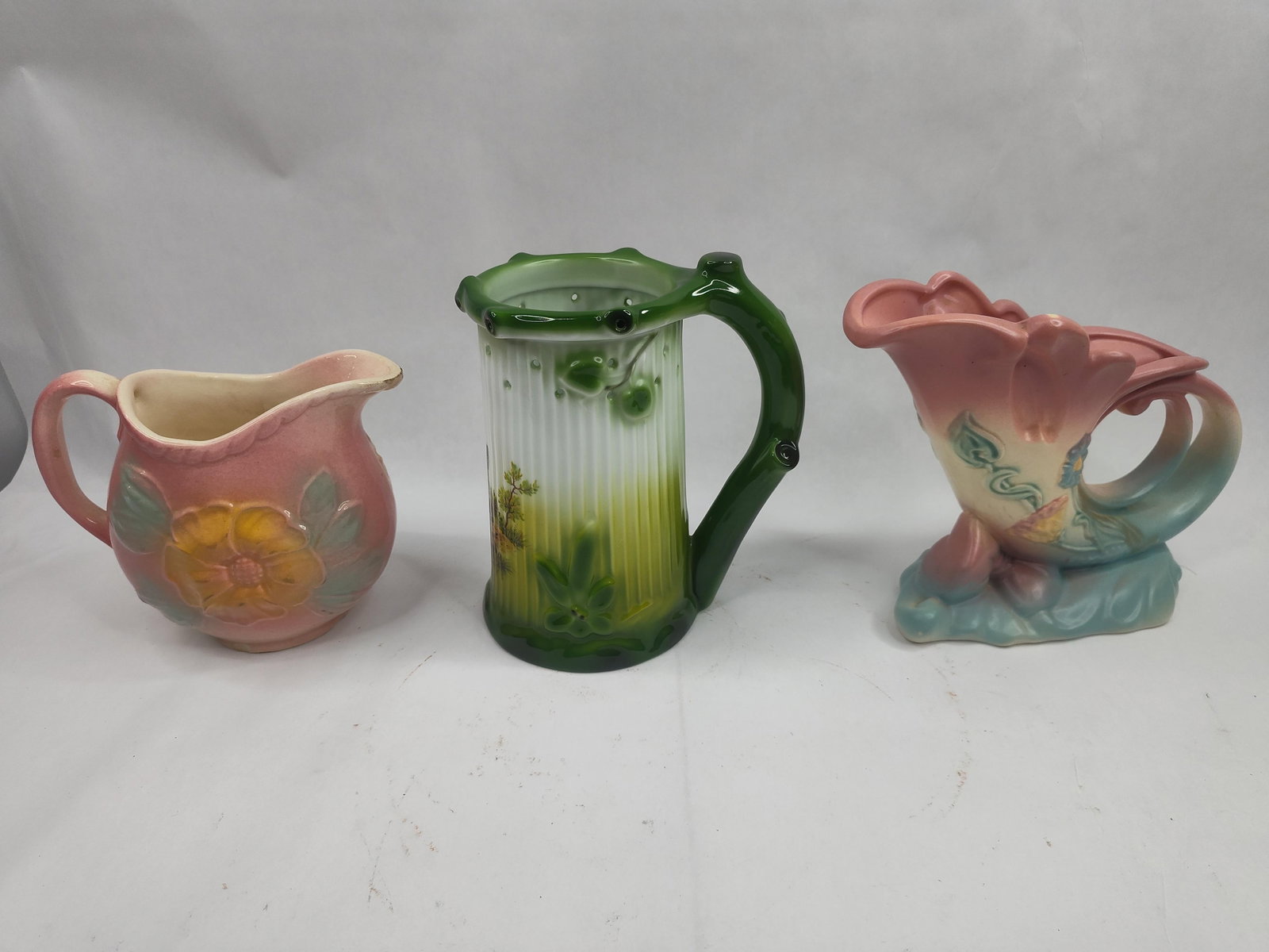 Hull & West Germany Porc. Vessels Set: This lot comprises three distinct ceramic vessels. The first is a pink matte-glazed West German porcelain pitcher featuring an embossed yellow flower with green leaves. The underside is incised with t
