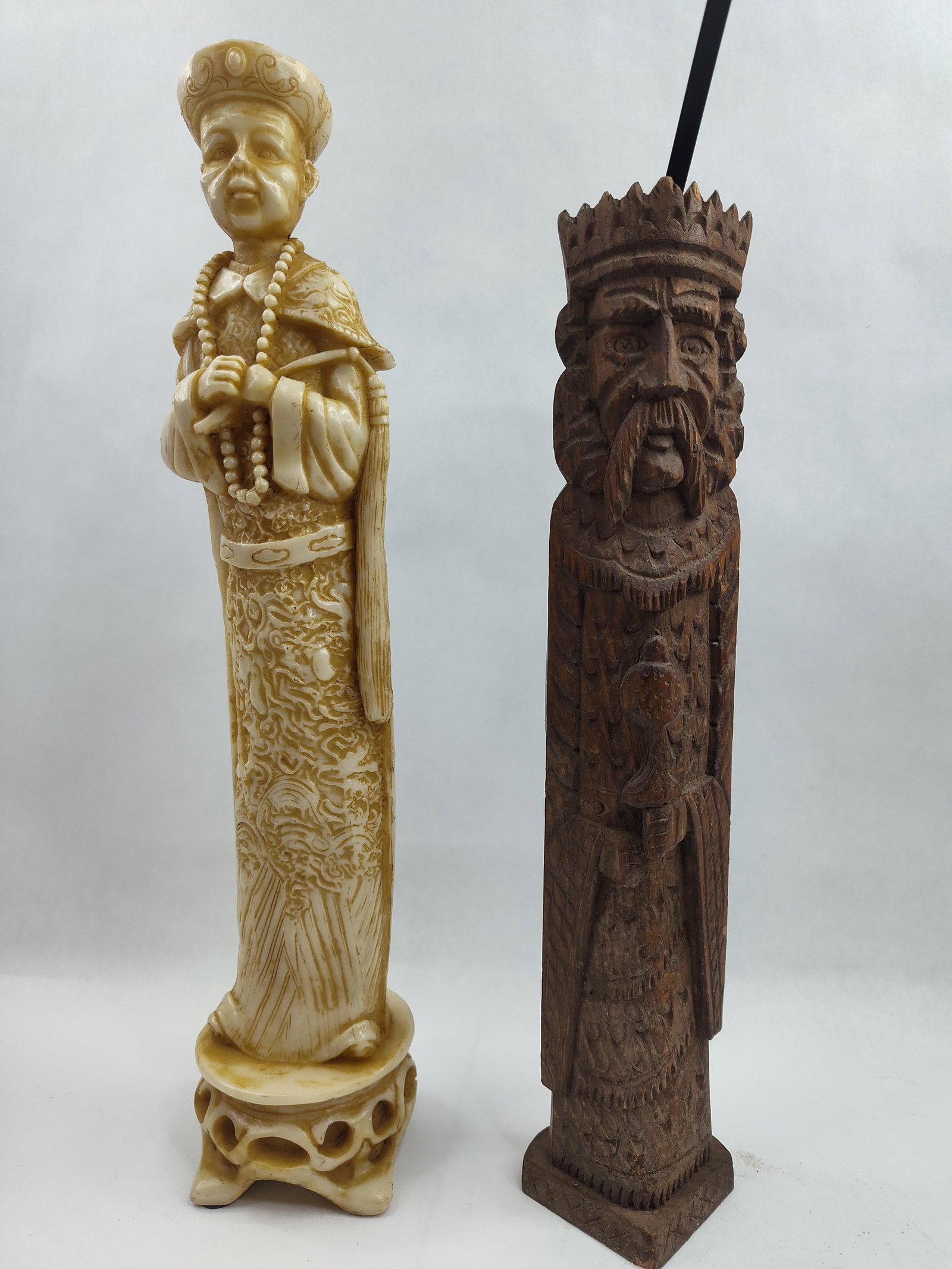 Pair Carved Figural Wood Sculptures: Two tall carved decorative figurines. The first is an ivory-colored resin or composition figure depicting a Chinese Qing Dynasty style emperor. The figure is shown wearing ornate traditional robes