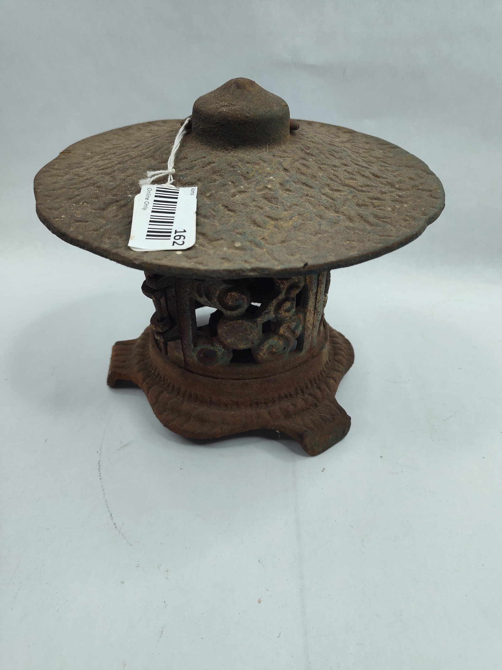 Japanese Cast Iron Pagoda Lantern: A cast iron Japanese style pagoda garden lantern with a weathered finish. The piece features a wide, circular roof with a textured, hammered surface and a central top finial. A metal wire handle is