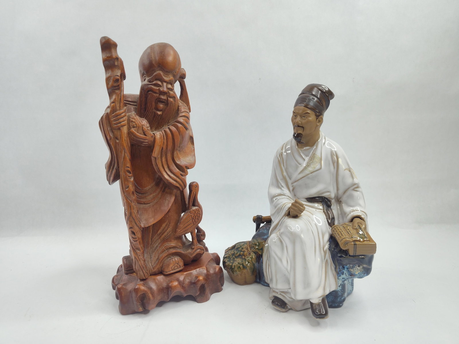 Pair Chinese Figures: Wood & Ceramic: A collection of two Asian-style decorative figurines. The first is a hand-carved wooden sculpture representing Shou Lao, the Chinese God of Longevity. The figure is depicted standing with an elongated