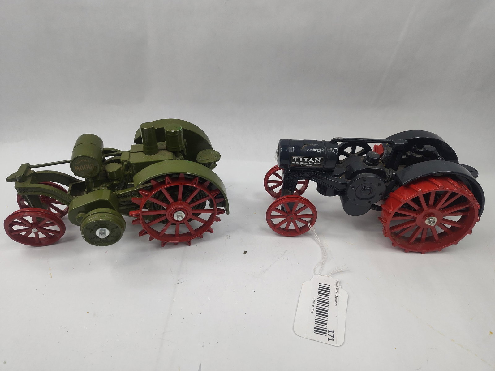 Pair Die-Cast Mogul & Titan Tractors: A pair of die-cast metal scale model tractors featuring painted enamel finishes. The first model is finished in olive green with red-spoked wheels and a horizontal cylinder engine. It features a