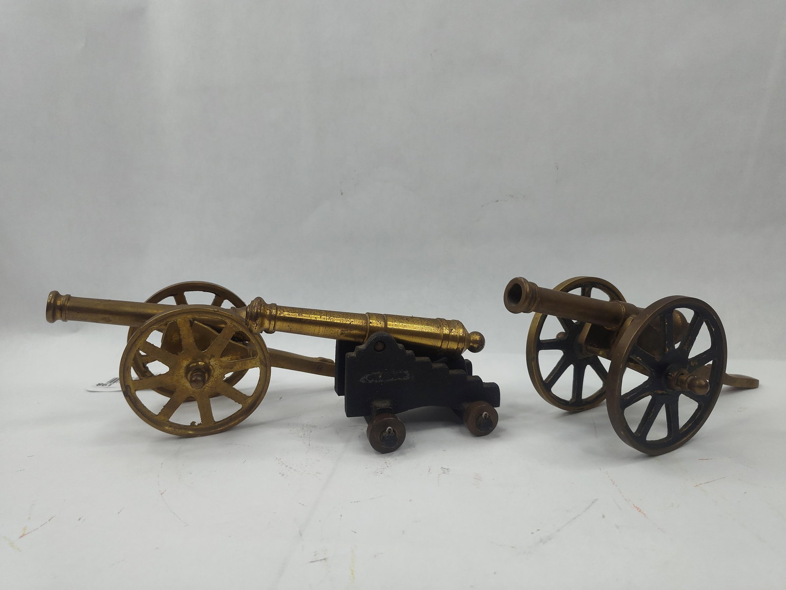 Set Brass & Cast Iron Mini Cannons: A collection of decorative miniature cannons featuring two distinct styles of carriage construction. The group consists of several field-style cannons and a single naval-style cannon. The field
