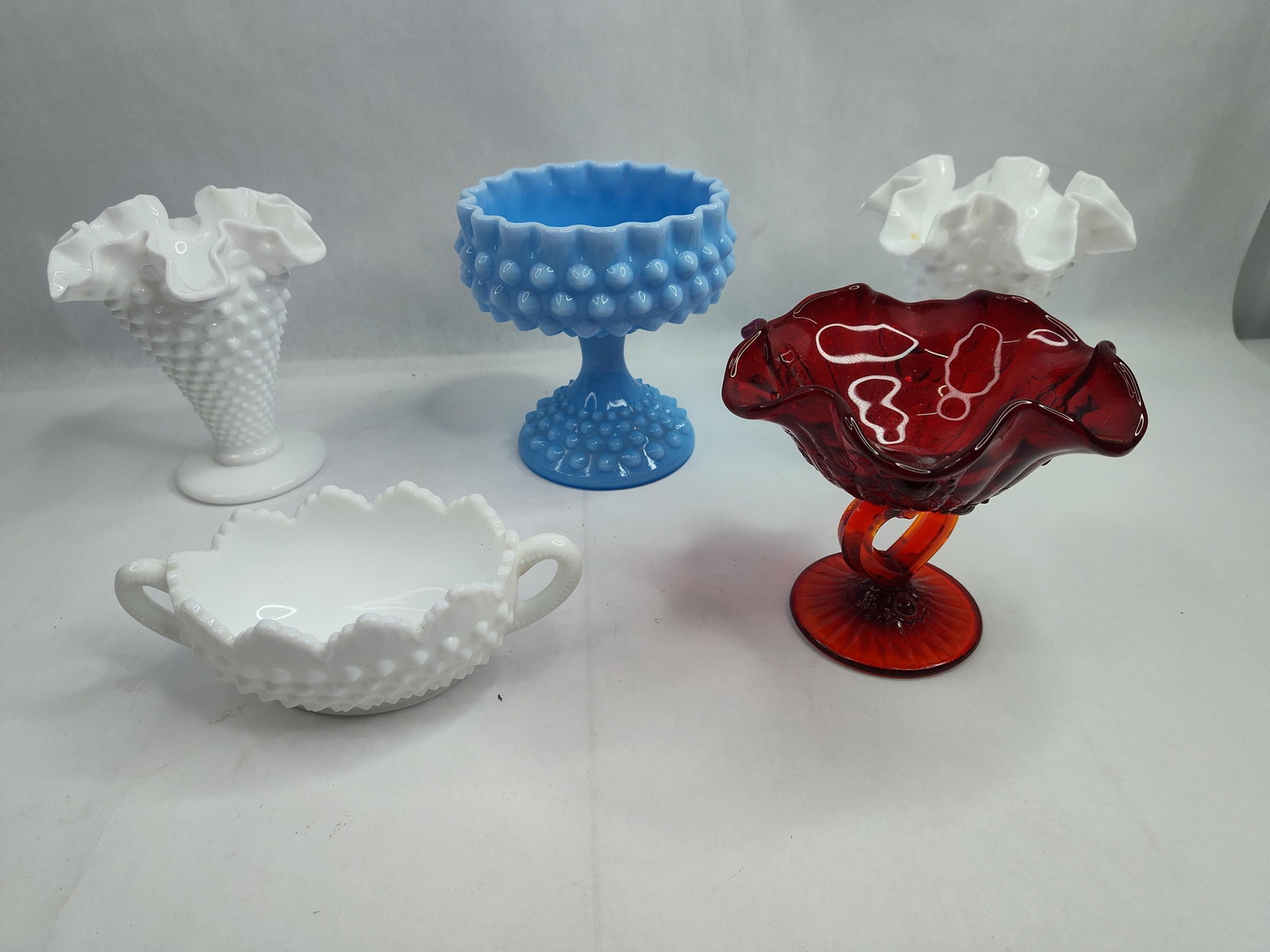 Group of American Glassware: An assortment of American decorative glassware, primarily featuring mid-20th-century pressed patterns. The collection includes three pieces of opaque white milk glass: a footed vase with a heavily ruf