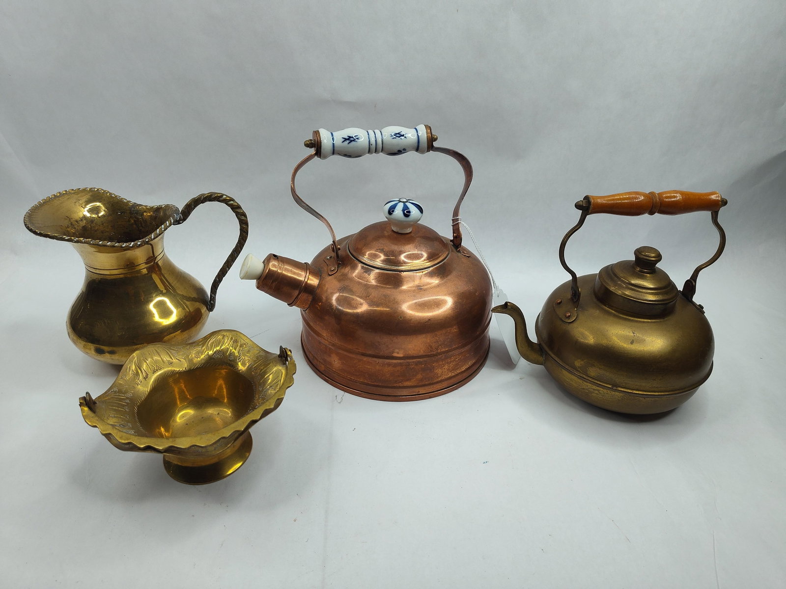 Collection of Copper & Brass Metalware: A collection of decorative and functional metalware comprising two teakettles, a pitcher, and a pedestal bowl. The primary piece is a copper teakettle featuring a hinged handle with a white porcelain