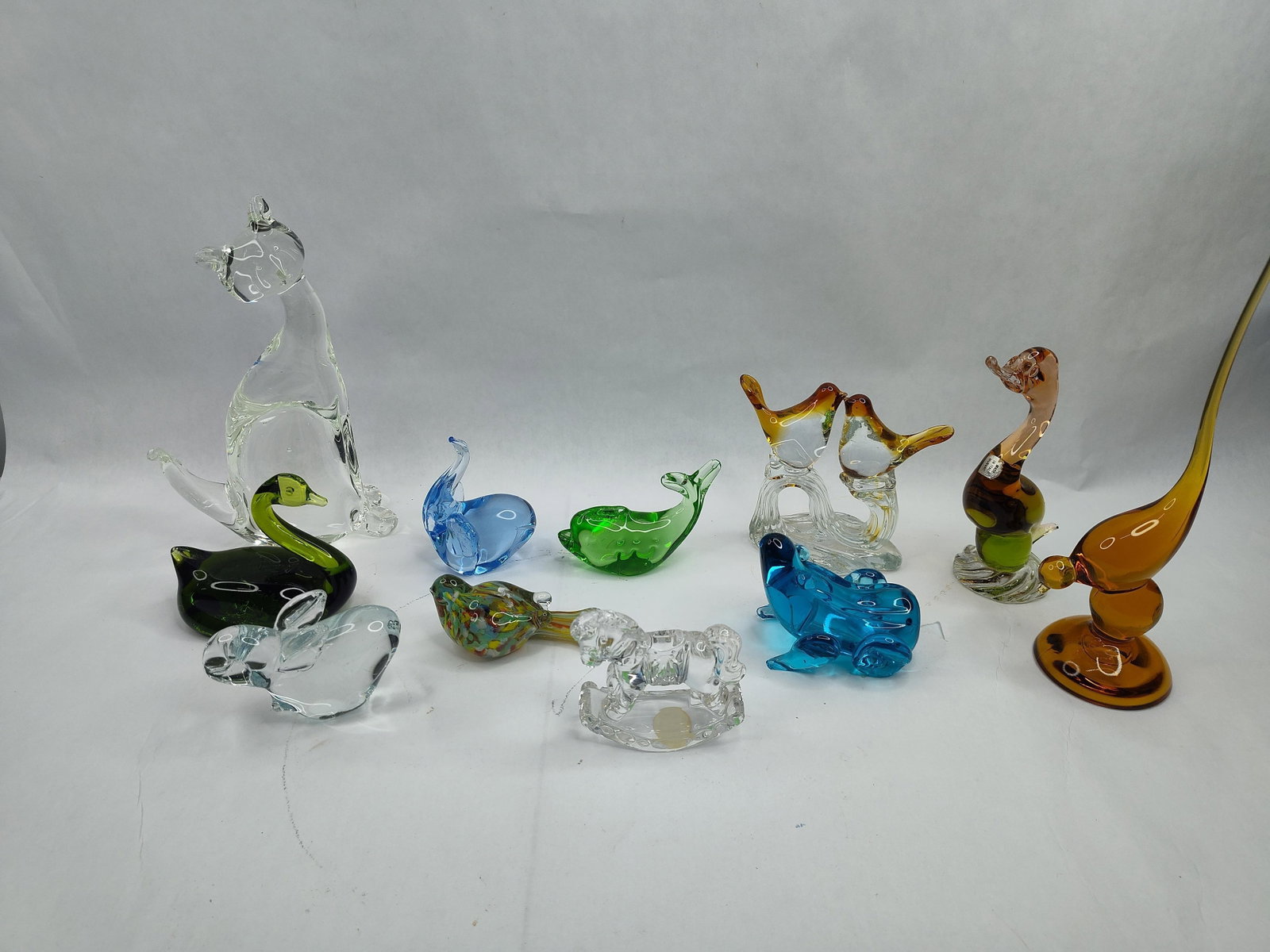 Murano & Blown Glass Animal Figurine: An assortment of hand-blown art glass animal figurines crafted in various colors and styles. The collection includes a tall colorless glass cat, a bicolored green and lime swan, a translucent blue