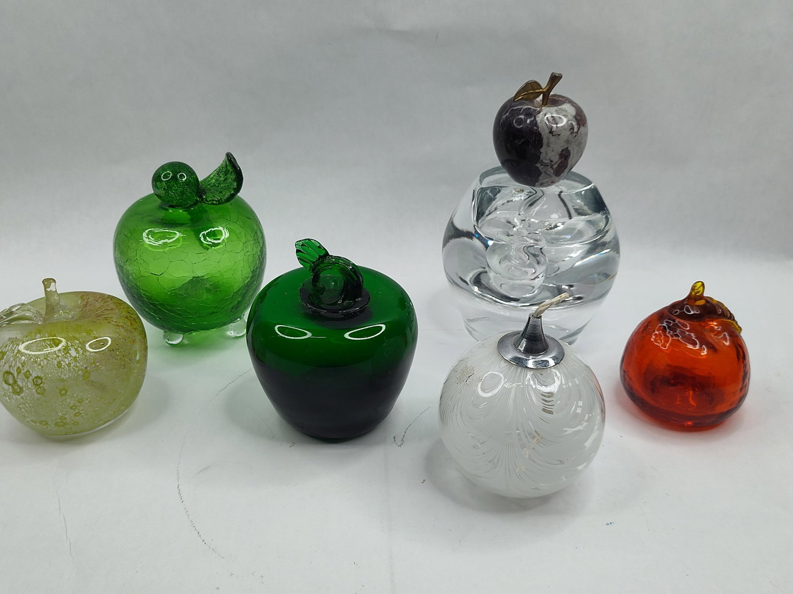 Set Art Glass & Stone Apple Objects: A collection of various decorative apple-themed objects utilizing multiple materials and glass-working techniques. The grouping features a clear glass paperweight of spherical form, topped with a