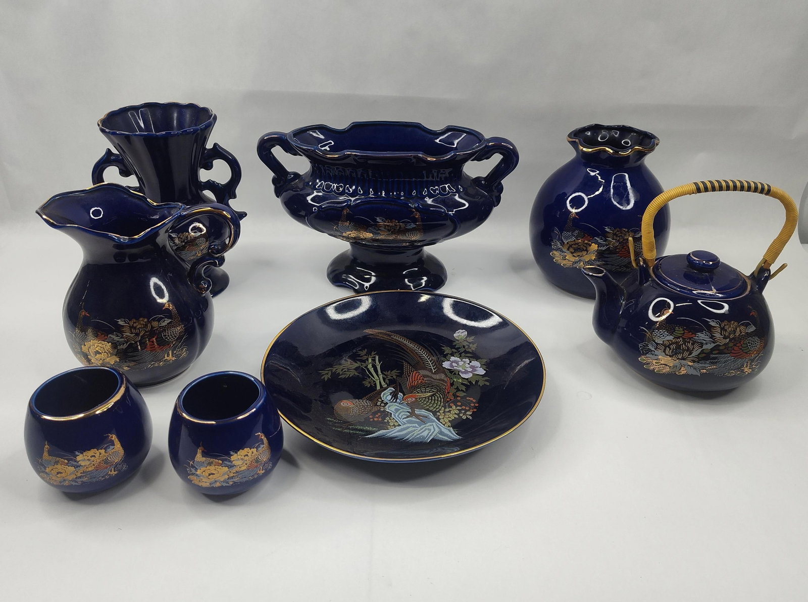Set Cobalt Blue Porc. Peacock Wares: A collection of porcelain decorative objects finished in a deep cobalt blue glaze and decorated with polychrome enamel and gilt highlights in a Peacock and Peony motif. The group includes a globular t