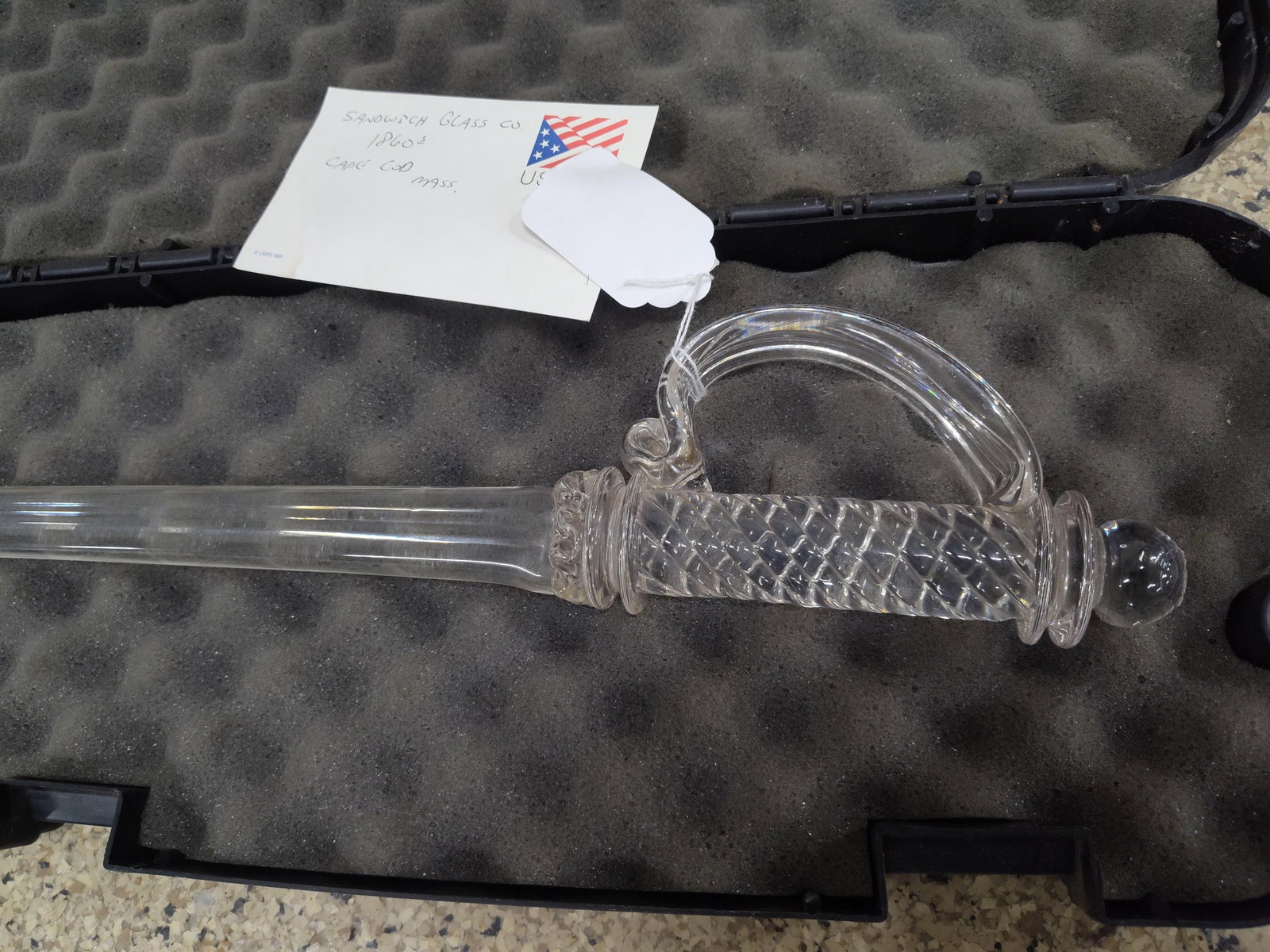 A Clear Glass Ceremonial Parade Sword: This lot consists of a ceremonial or parade sword crafted entirely of clear glass. The piece features a single-edged blade that tapers to a point, joined to a decorative hilt. The hilt is composed of 