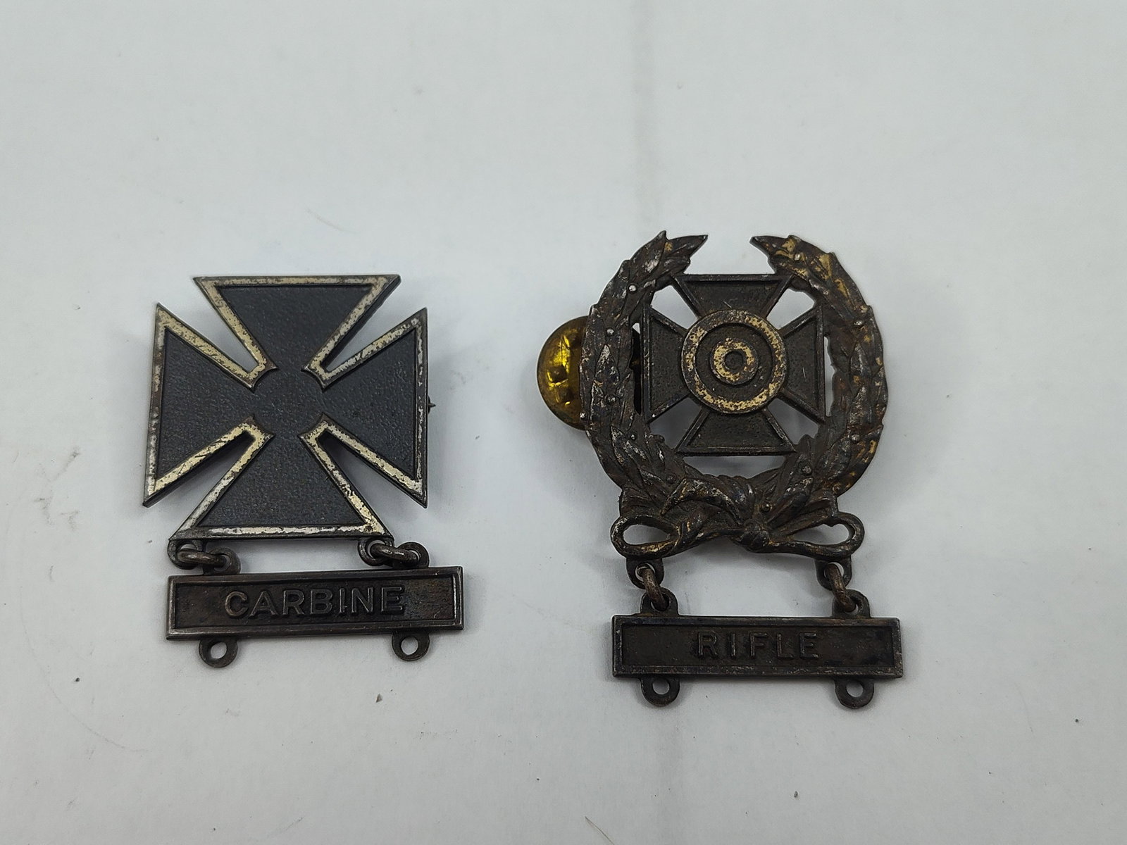 Pair Str. US Military Marksmanship Bgs: This lot comprises two United States military marksmanship qualification badges constructed from silver-colored metal. The first is a Sharpshooter badge featuring a cross patee within a laurel