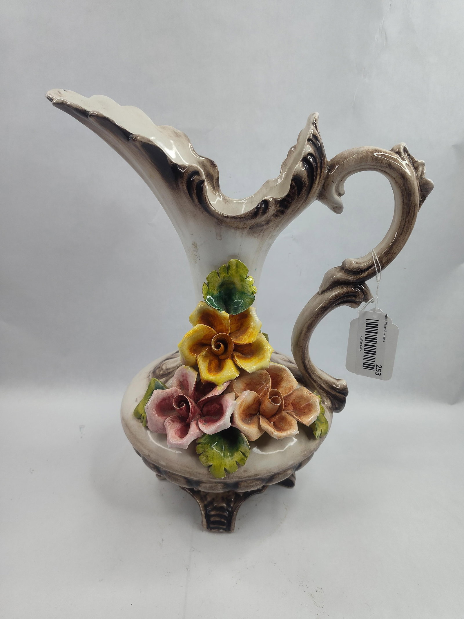 Capodimonte Ceramic Floral Pitcher: This Italian ceramic pitcher is designed in a Rococo style, featuring a cream-colored glazed body with hand-applied high-relief floral motifs and brown shaded accents. The form includes a flared,