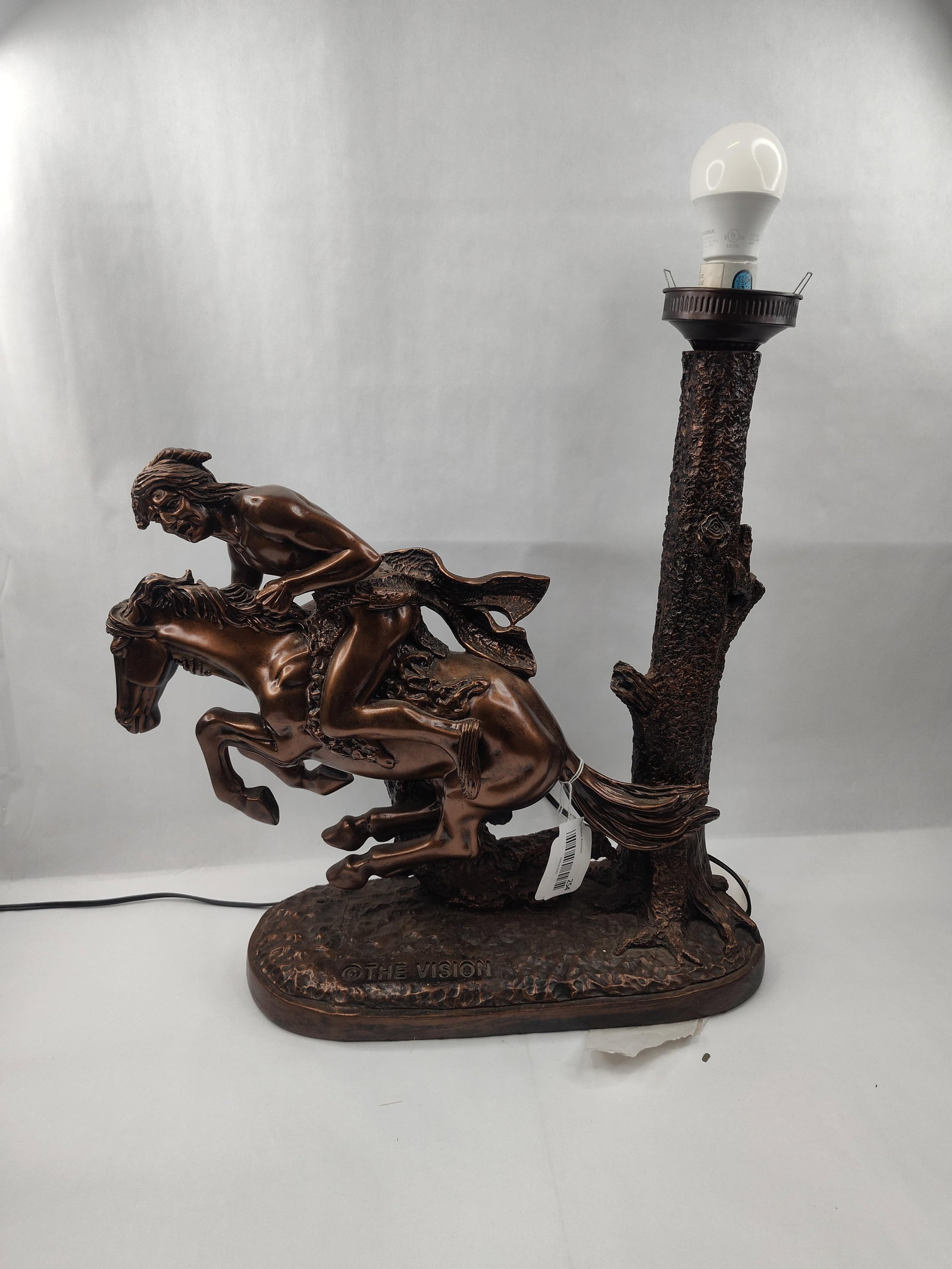 Vision Cast Resin Equestrian Lamp: This table lamp features a cast resin figural sculpture with a metallic faux-bronze finish. The dynamic composition depicts a Native American man riding a horse that is in a rearing or bucking